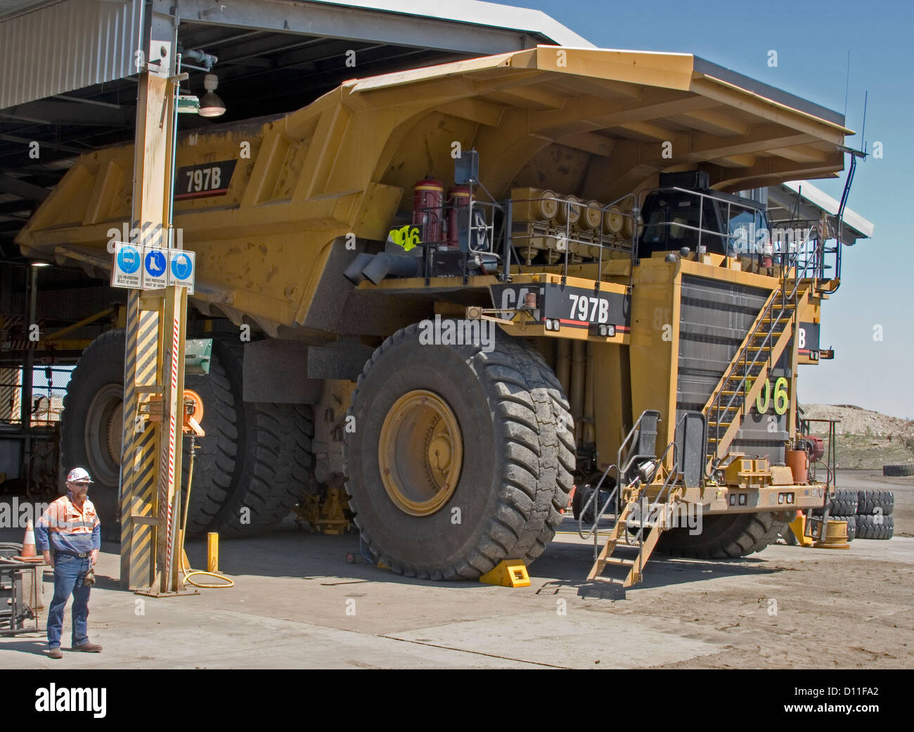 Mine worker / truck driver dwarfed by huge mining dump truck in workshop at open cut coal mine in central Queensland Australia Stock Photo