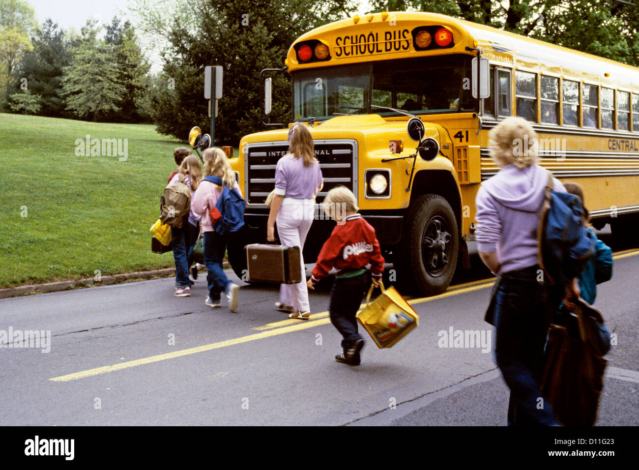 1980s ELEMENTARY AND MIDDLE SCHOOL STUDENTS BOARDING SCHOOL BUS CROSSING HIGHWAY Stock Photo