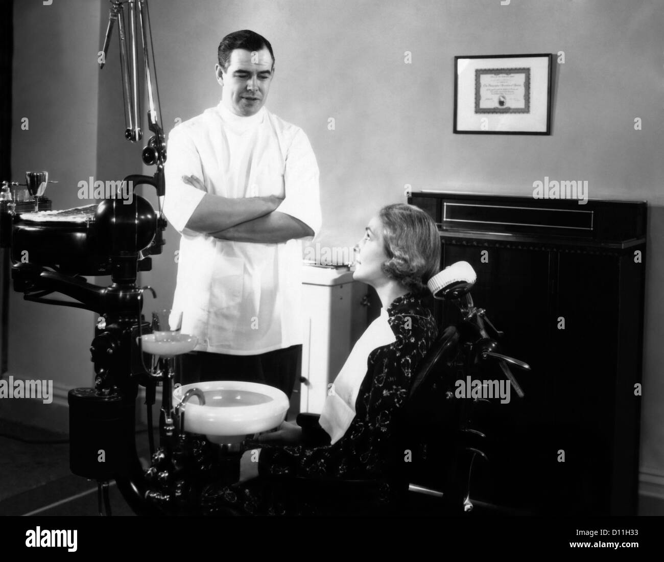 1930s 1940s MAN DENTIST ARMS CROSSED TALKING TO WOMAN PATIENT SITTING IN DENTAL CHAIR Stock Photo