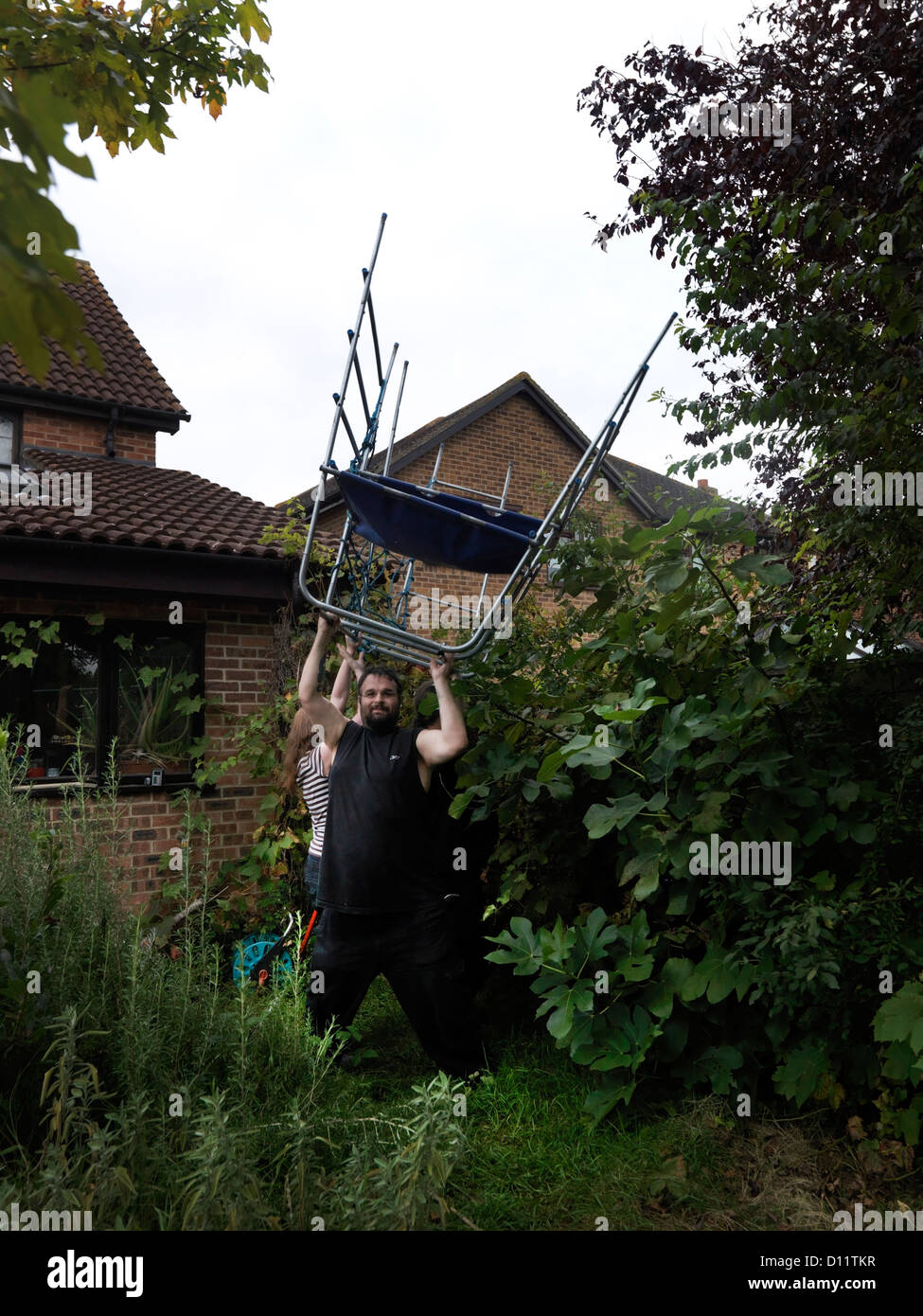 Family Moving House Father Lifting Up Trampoline Above His Head Taking It Out Of Garden England Stock Photo