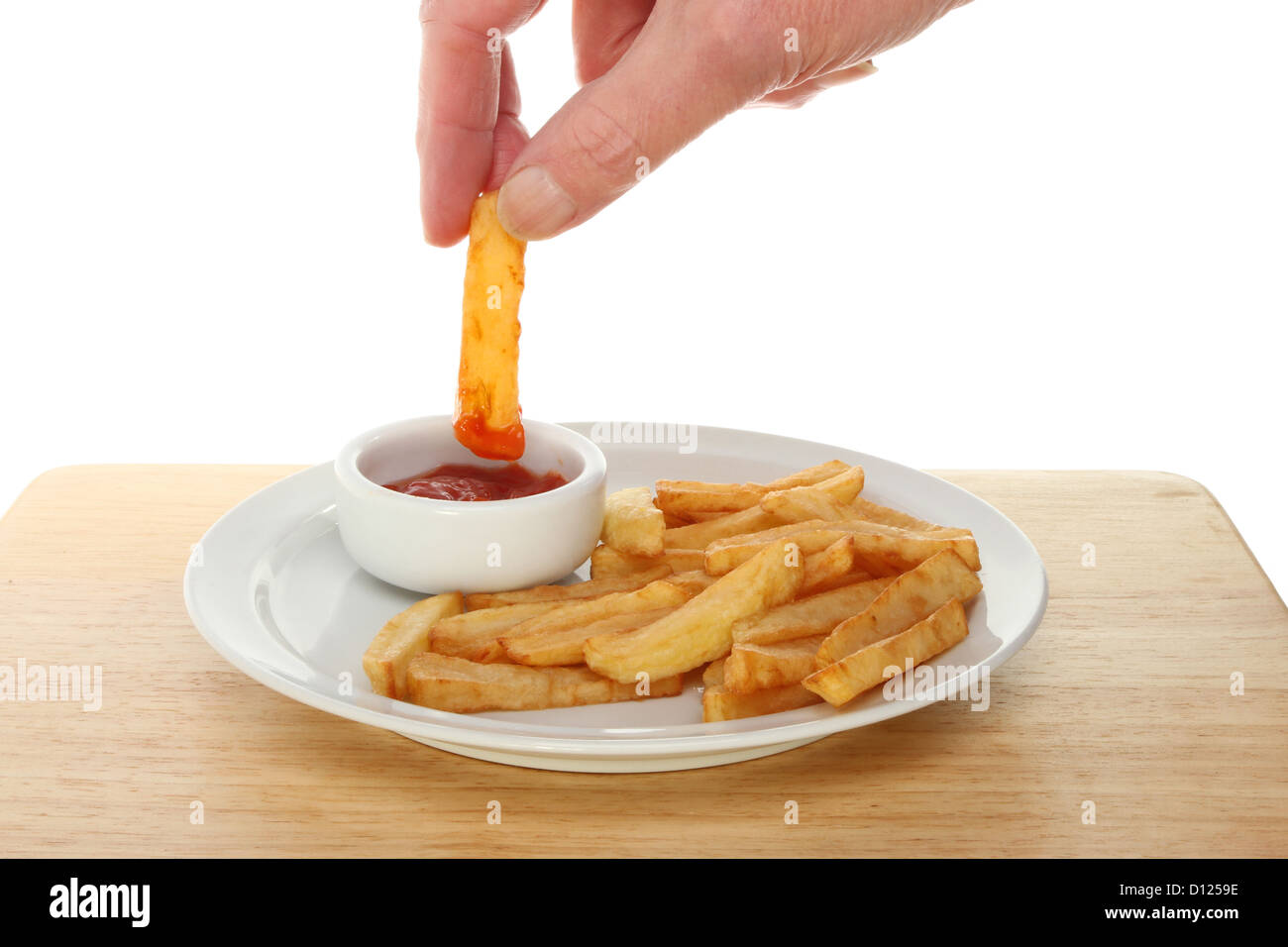 Hand dipping a potato chip into tomato ketchup in a ramekin next to chips on a plate Stock Photo