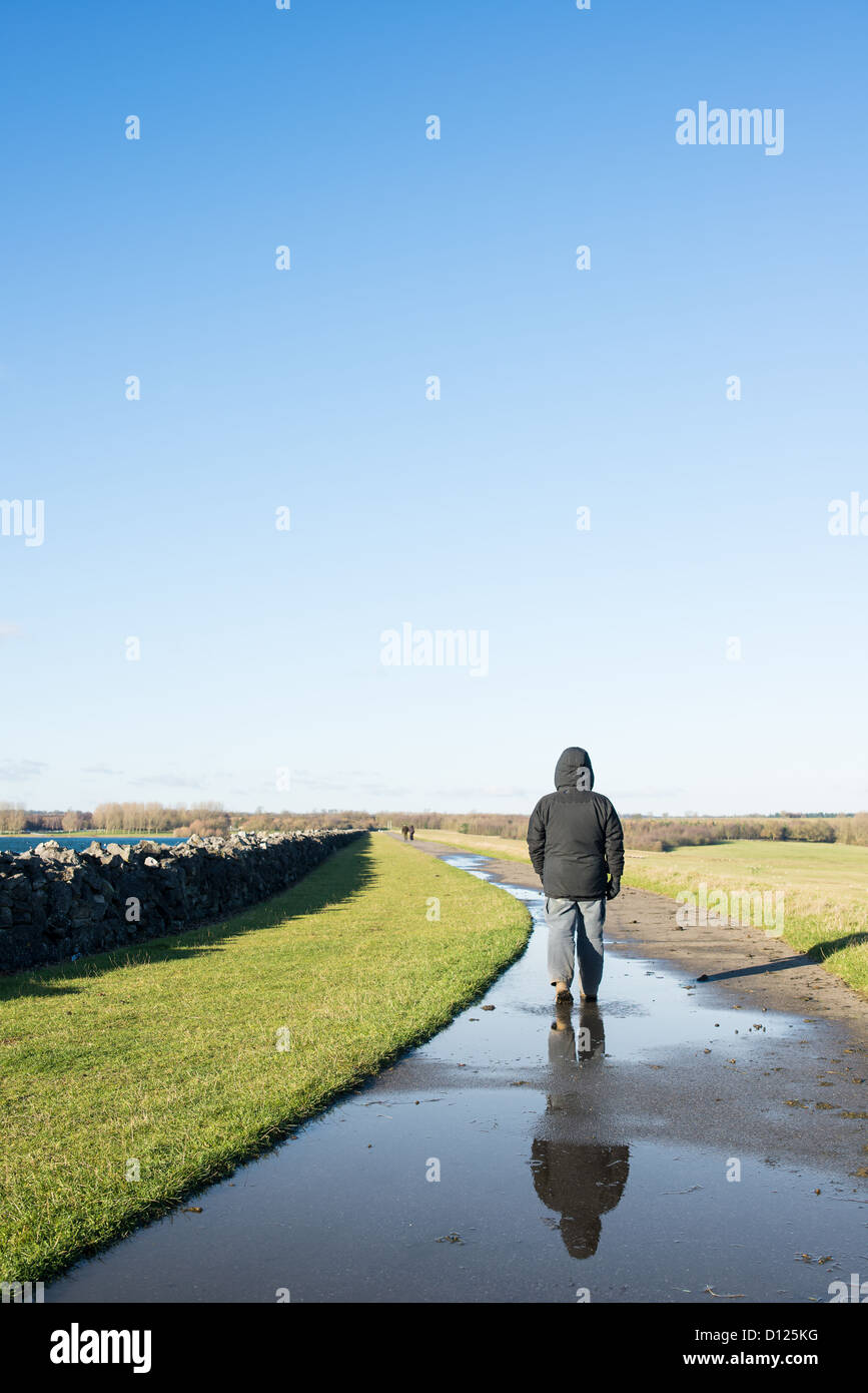 Solitary walker striding out on a wet path on a cold, wet, sunny winter's day. Stock Photo