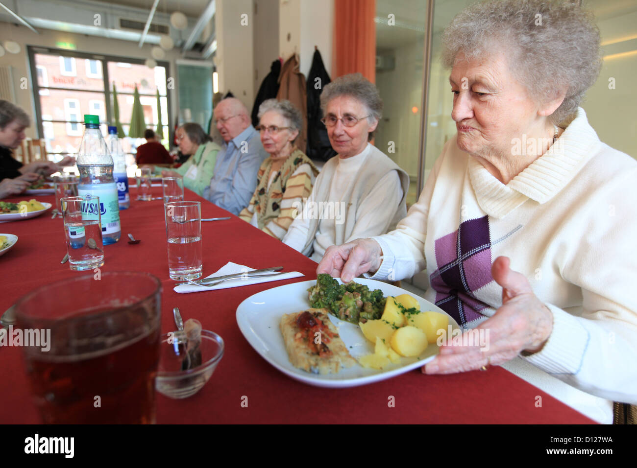Elderly women and men eat and drink together during a communal meal in