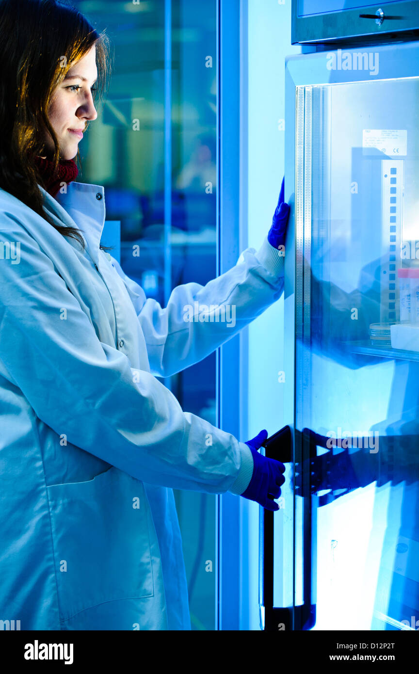Young female scientist in science lab standing by specimen fridge Stock Photo
