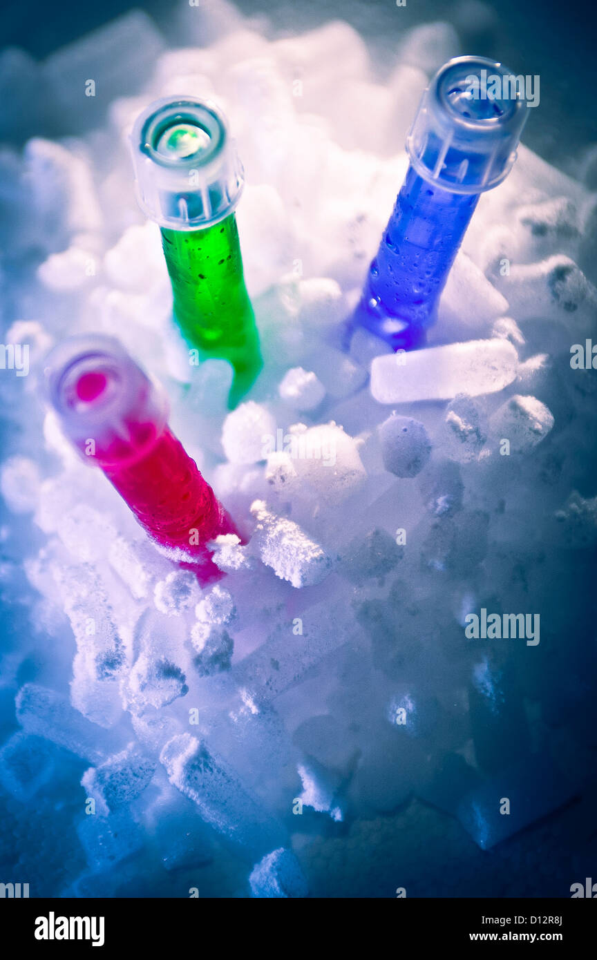Three test tubes containing bright red, green and blue liquid nest in dry ice in science laboratory Stock Photo