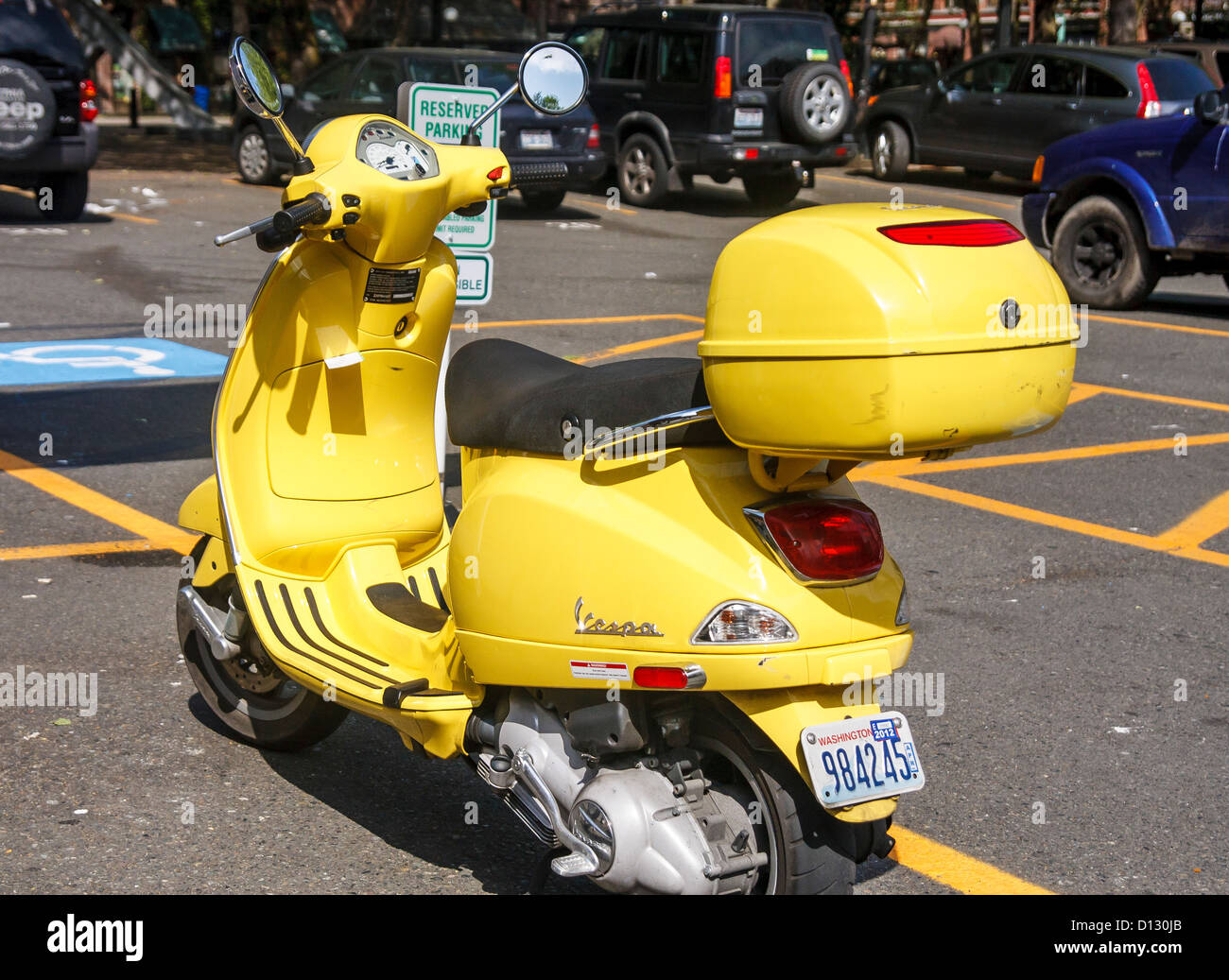 A yellow Vespa scooter in a parking lot Stock Photo
