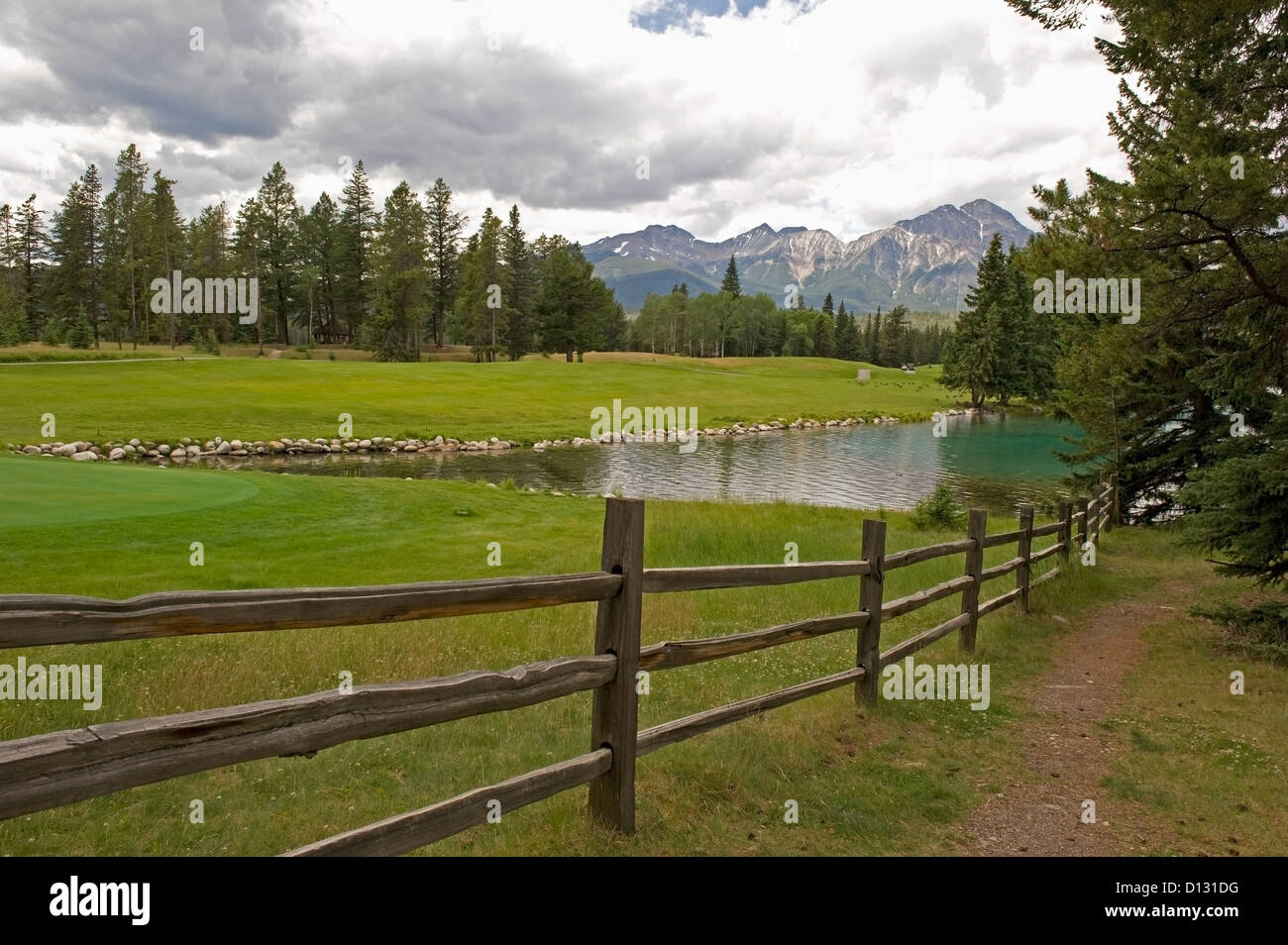 Green Grass Field Lake With The Mountains In The Distance; Alberta Canada Stock Photo