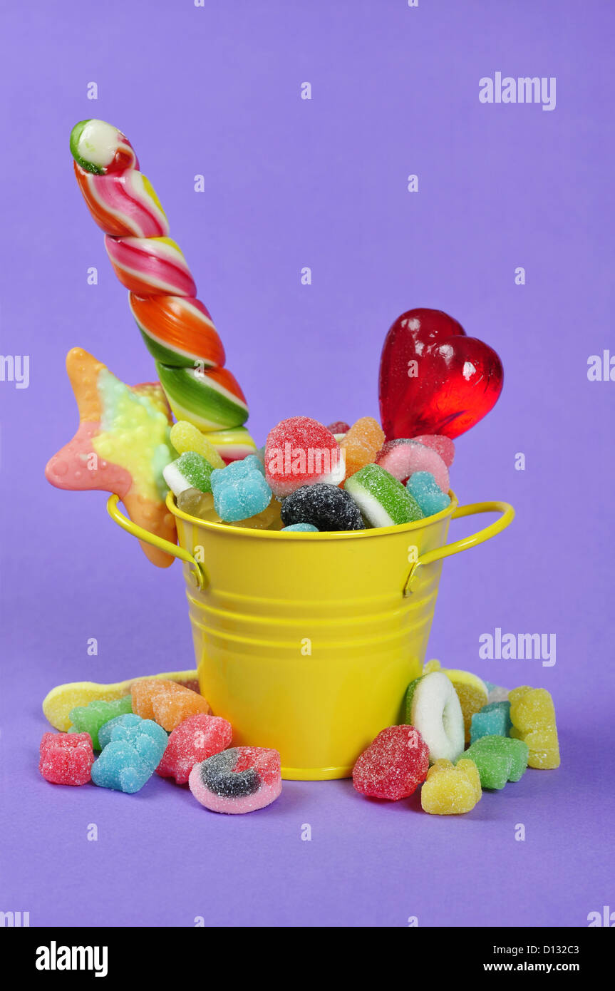 Colorful candies in yellow bucket on purple background Stock Photo