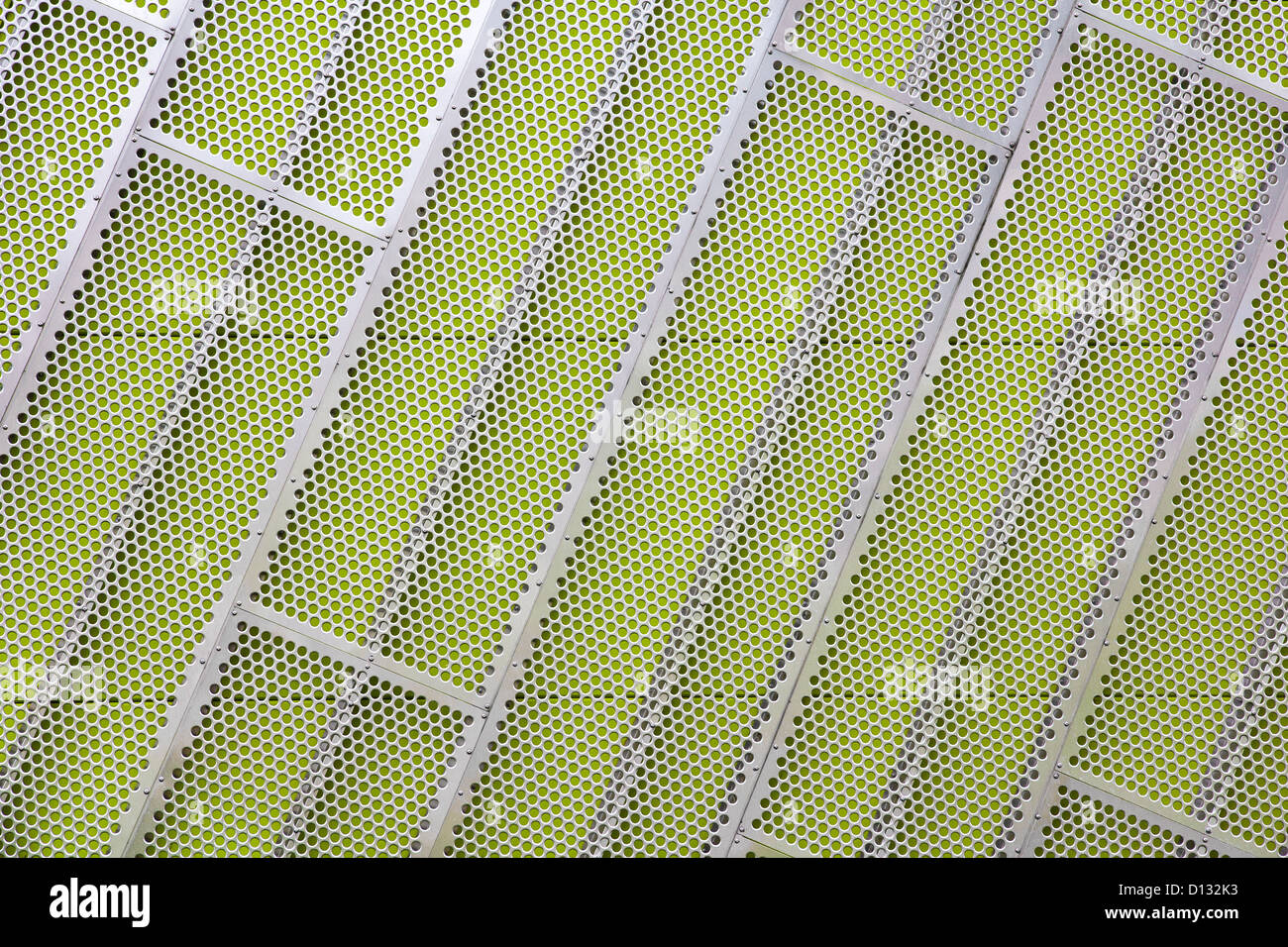 Steel facade cladding with a mesh of holes on a green wall Stock Photo
