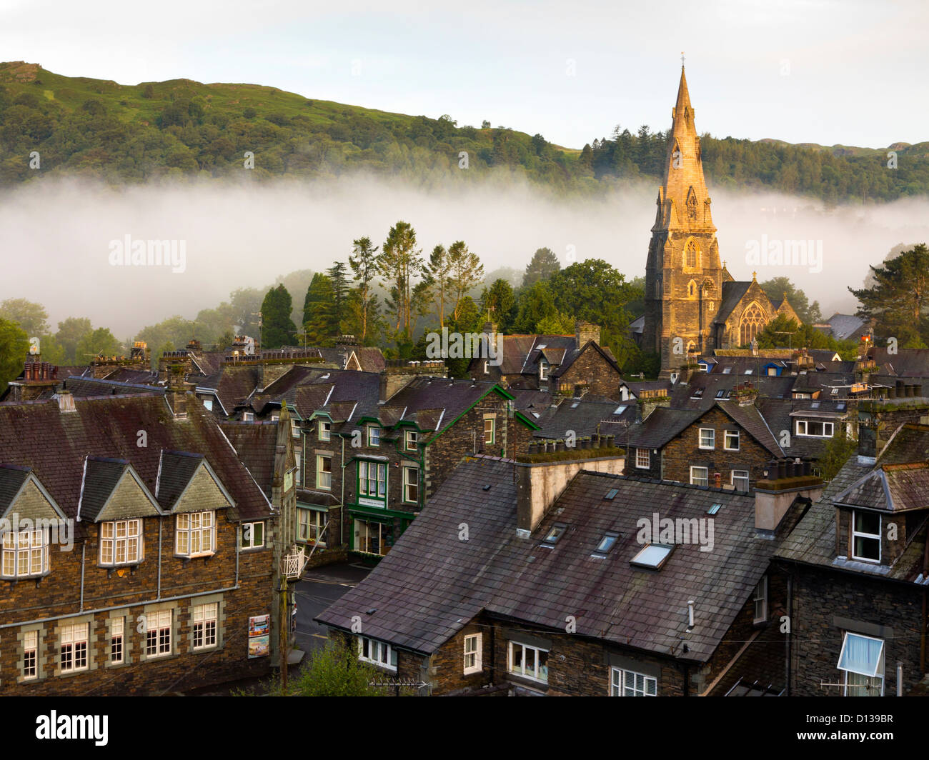 View across rooftops towards the church and early morning mist in Ambleside Cumbria Lake District National Park England UK Stock Photo