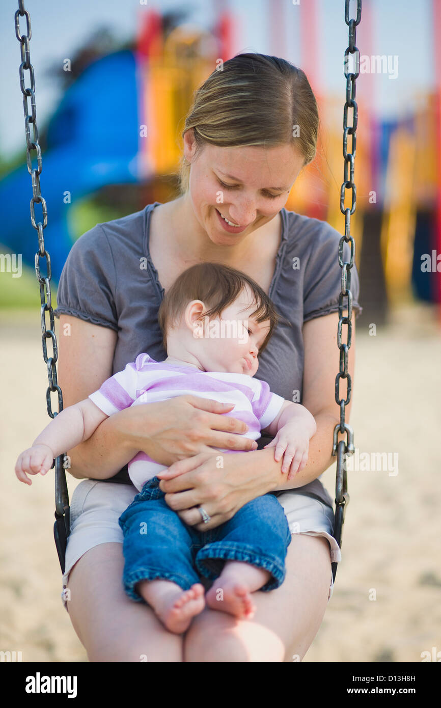Woman In Her Late 20's Sitting On A Swing Holding Her 6-Month-Old Daughter In A Park; Ontario Canada Stock Photo