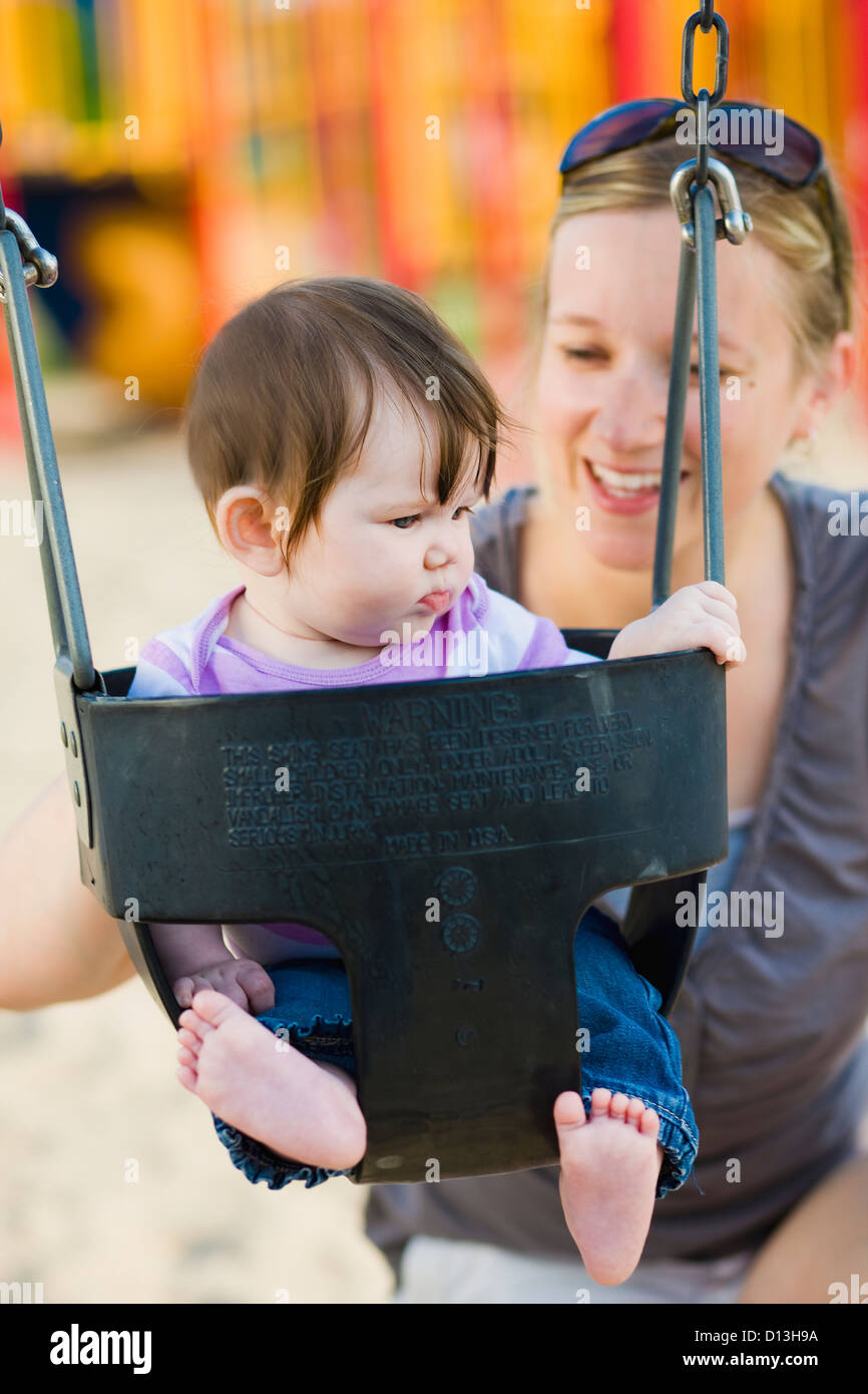 Woman In Her Late 20's In A Park With Her 6-Month-Old Daughter In A Swing; Ontario Canada Stock Photo