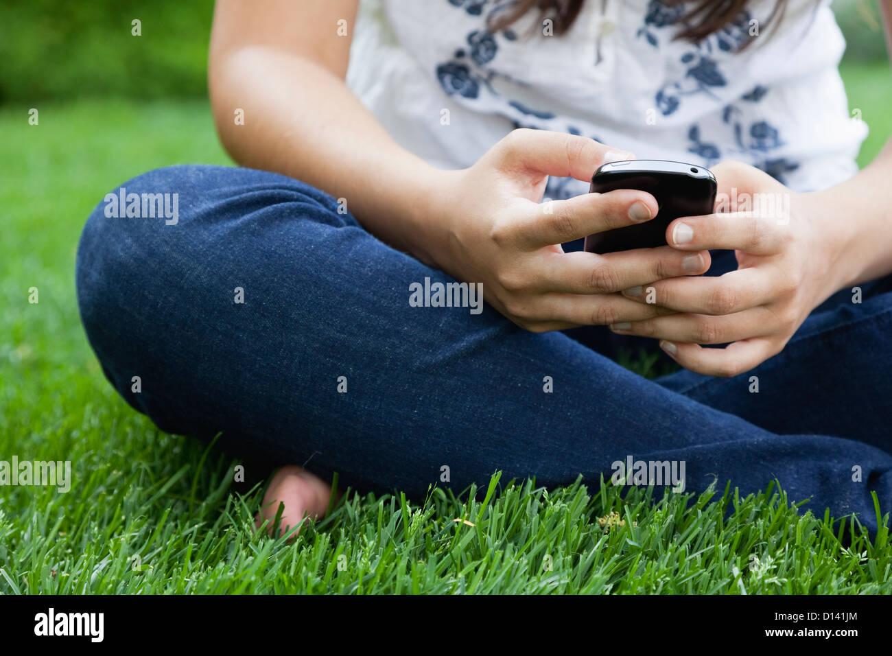 USA, Illinois, Metamora, Young woman texting on his mobile while sitting on grass Stock Photo