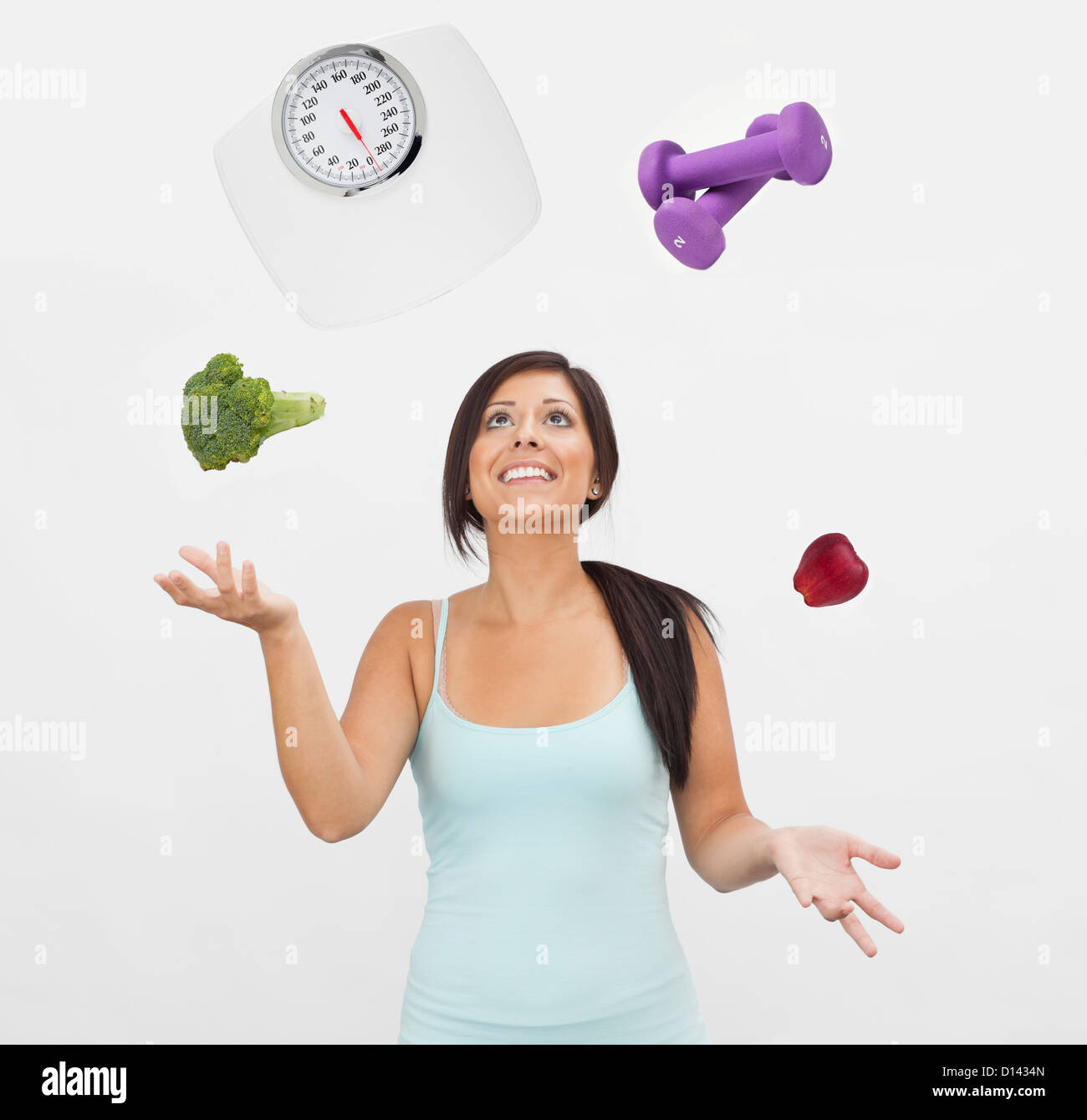 Studio shot of young woman juggling with weight scale, weights, fruit