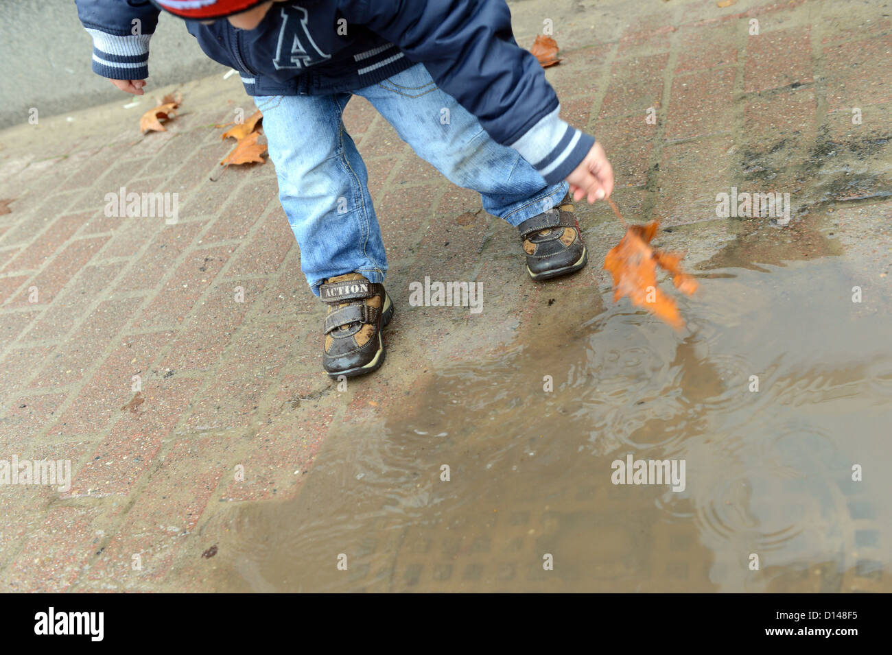 A child plays in a puddle at a childrens' nursery school in Berlin, Germany, 30 November 2012. Photo: Jens Kalaene Stock Photo