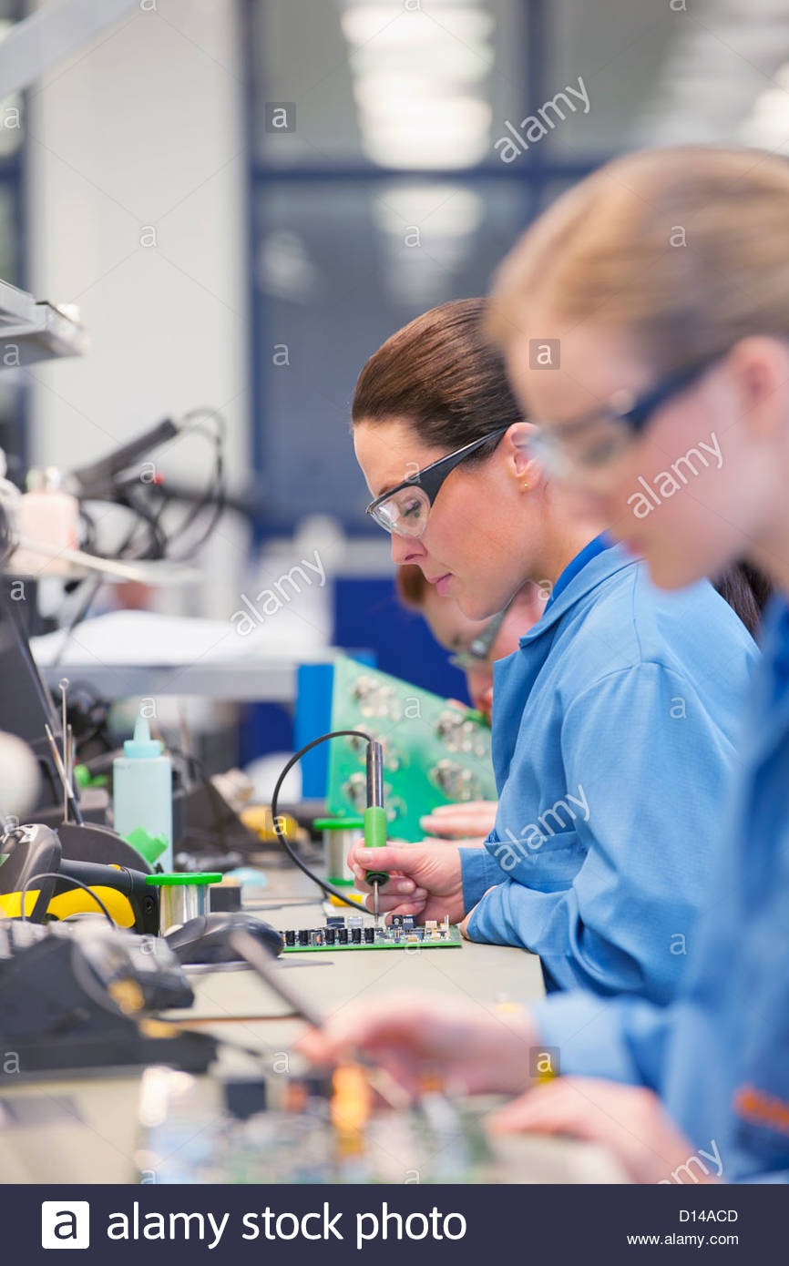 technicians soldering circuit boards on production line in stocktechnicians soldering circuit boards on production line in manufacturing plant