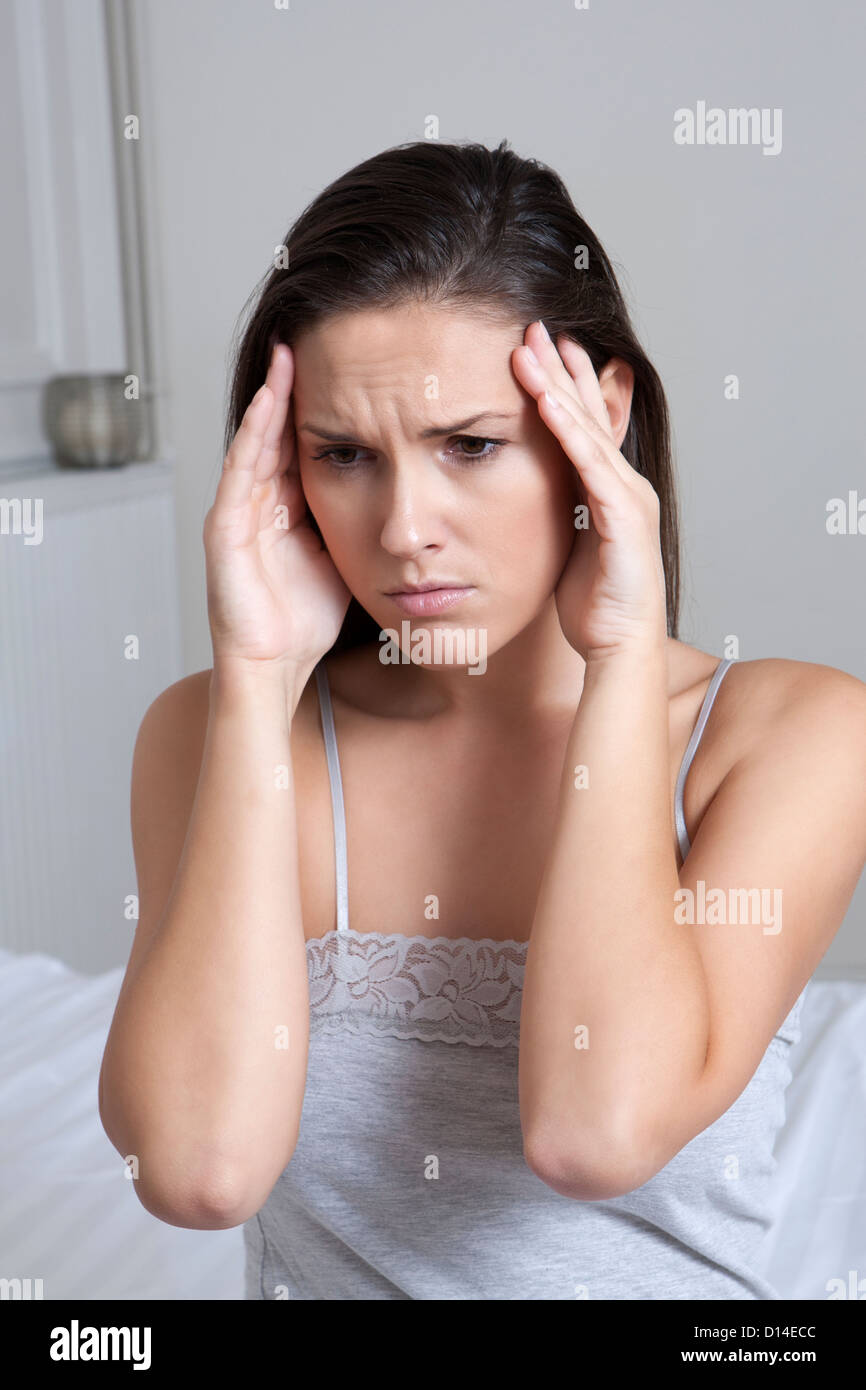 Woman rubbing her temples on bed Stock Photo