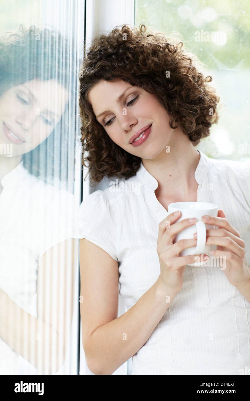 young woman standing by the window with cup of coffee Stock Photo