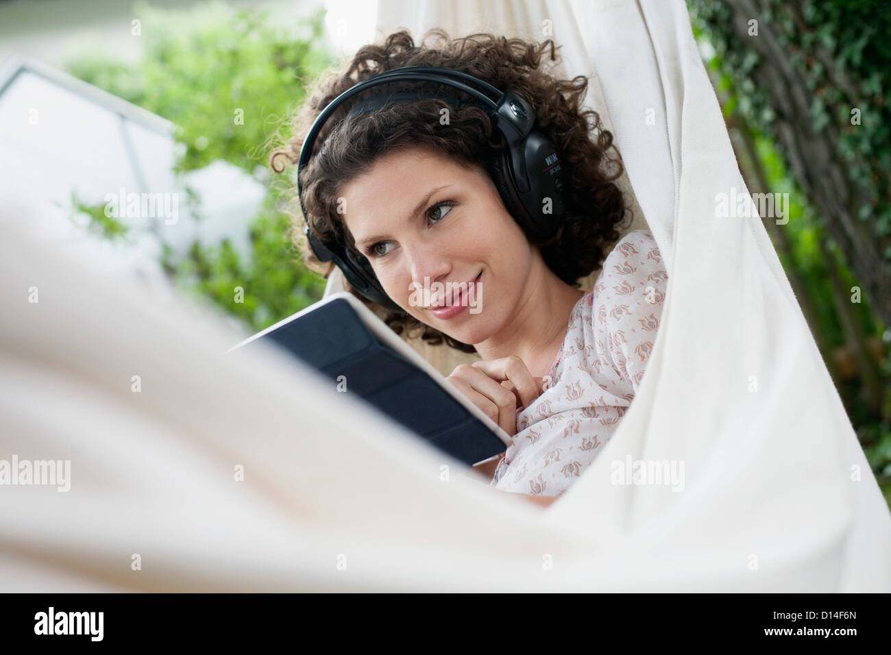 young woman in hammock in garden with earphones and tablet computer Stock Photo