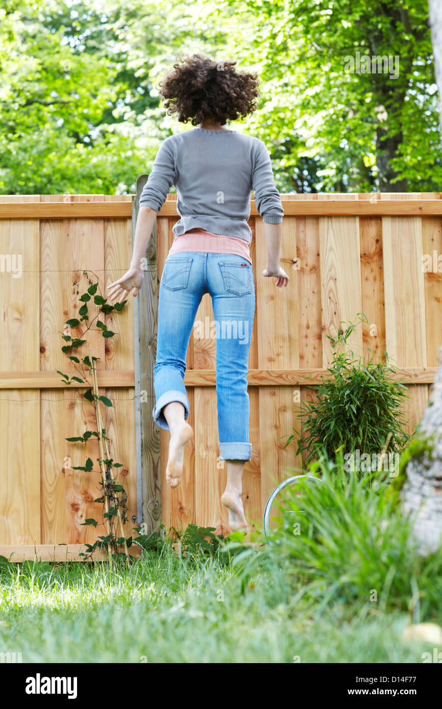 young woman in garden trying to look over the fence Stock Photo