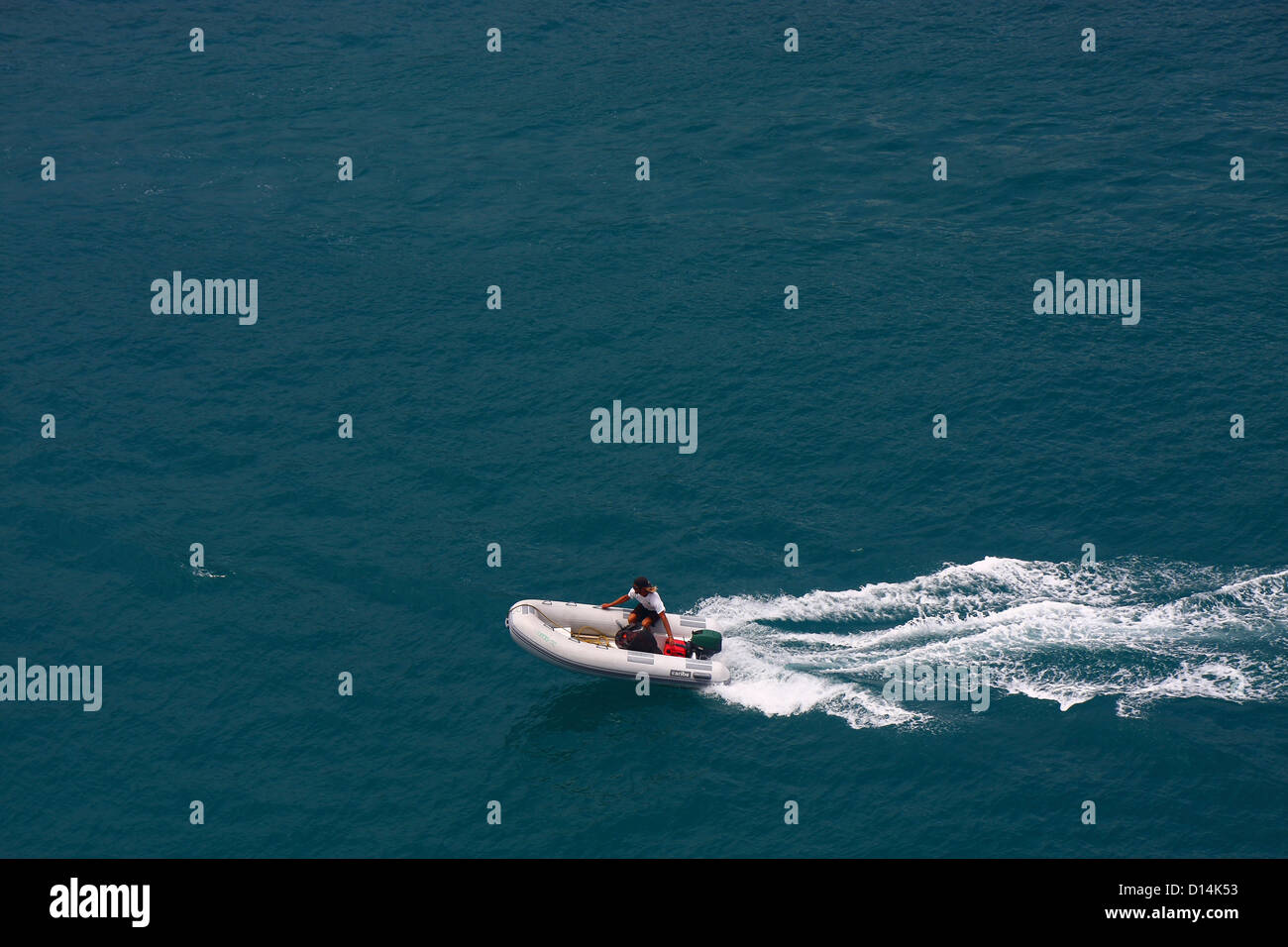 A man speeding across aqua water in a rubber dinghy Stock Photo - Alamy