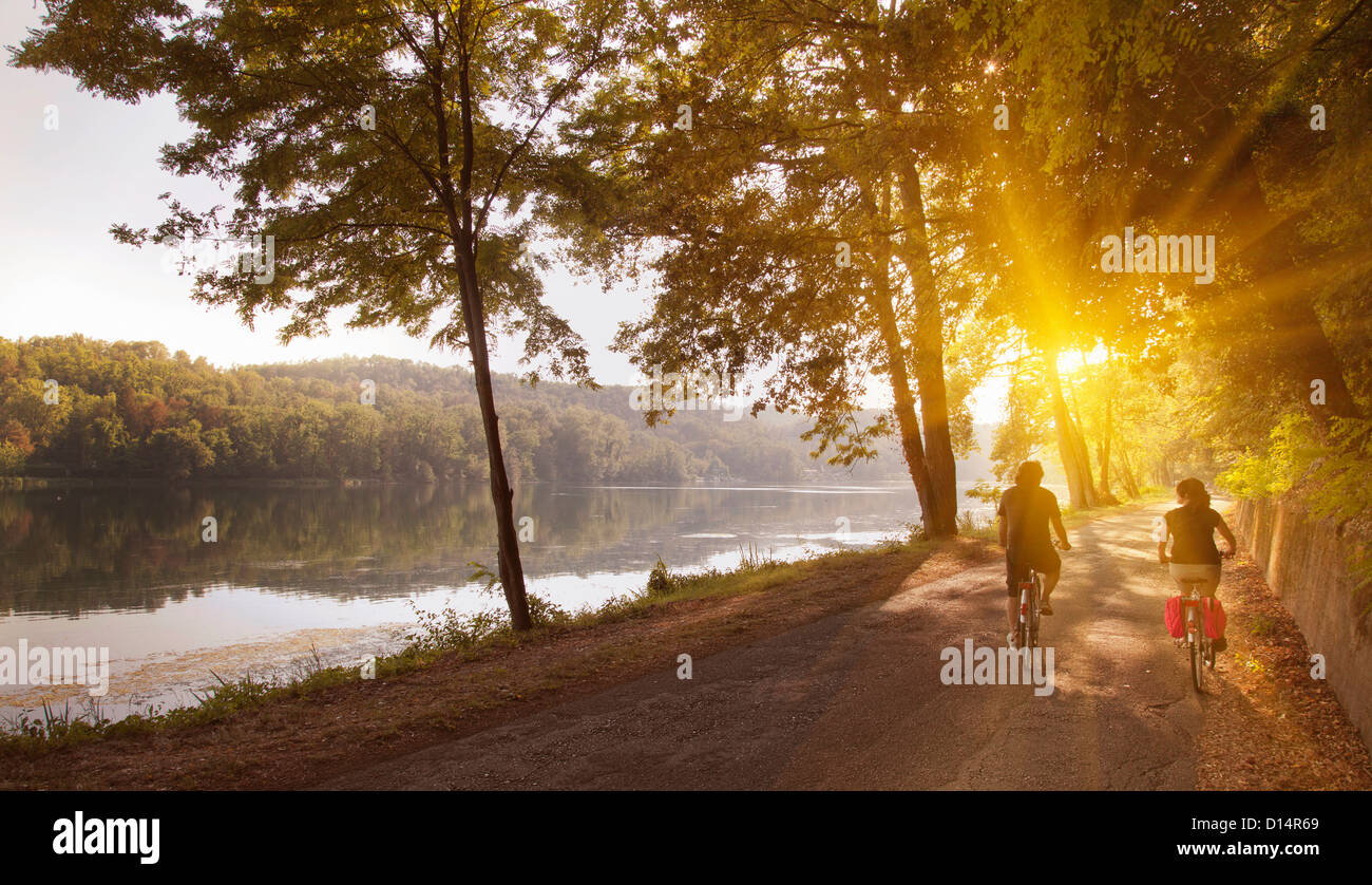 Couple riding bicycles by river bank Stock Photo