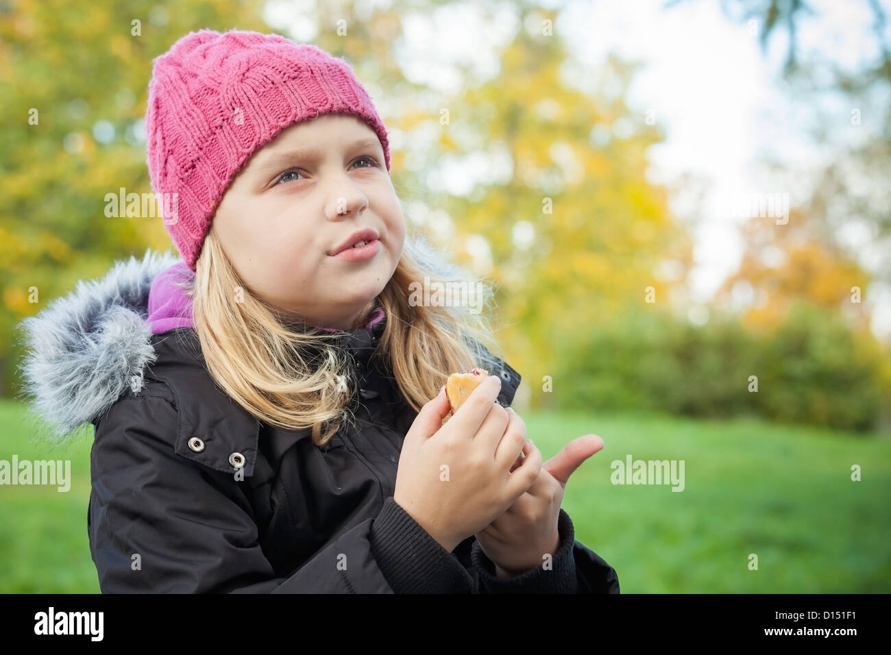little beautiful blond girl eating cake and thinking about something. Outdoor portrait. Stock Photo