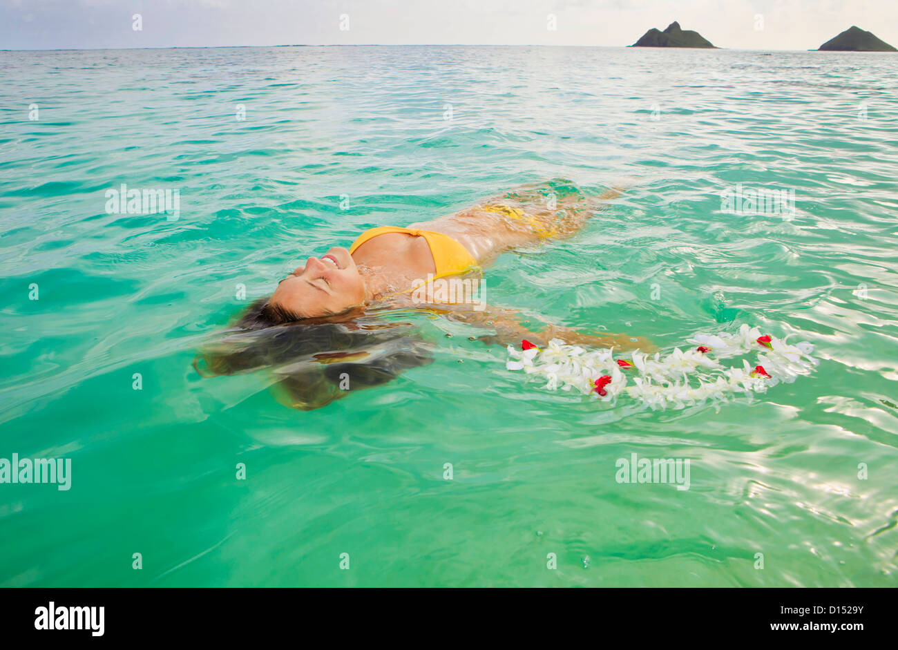 Hawaii, Oahu, Lanikai, Young Woman Floating In Tropical Ocean Water With Lei. Stock Photo
