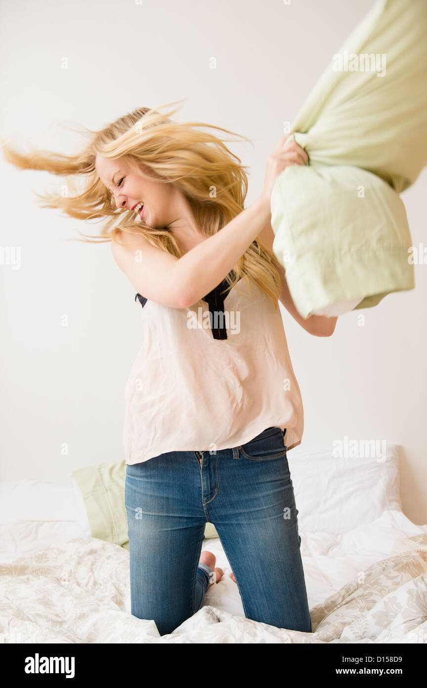USA, New Jersey, Jersey City, Young woman kneeling on bed and throwing