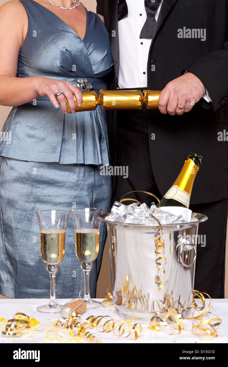 A couple in evening dress pulling a gold Christmas cracker at a Champagne party. Stock Photo