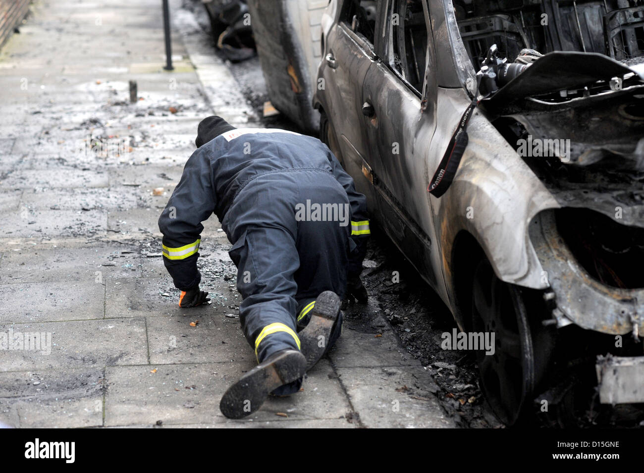 A fire investigation officer on hands and knees looking at burnt out cars in Connaught Road Hove Stock Photo