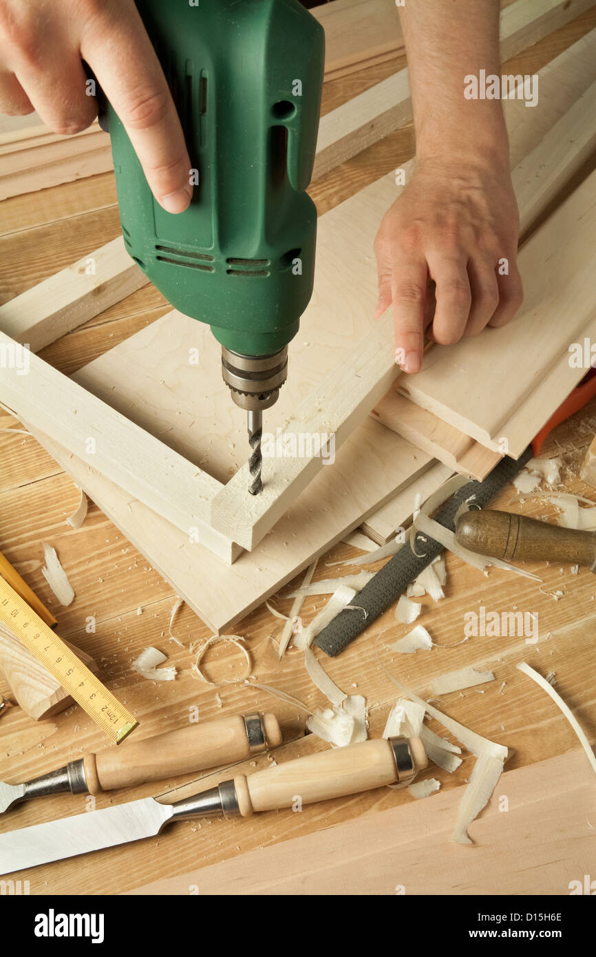 Wooden workshop table with tools. Man's arms drill plank. Stock Photo