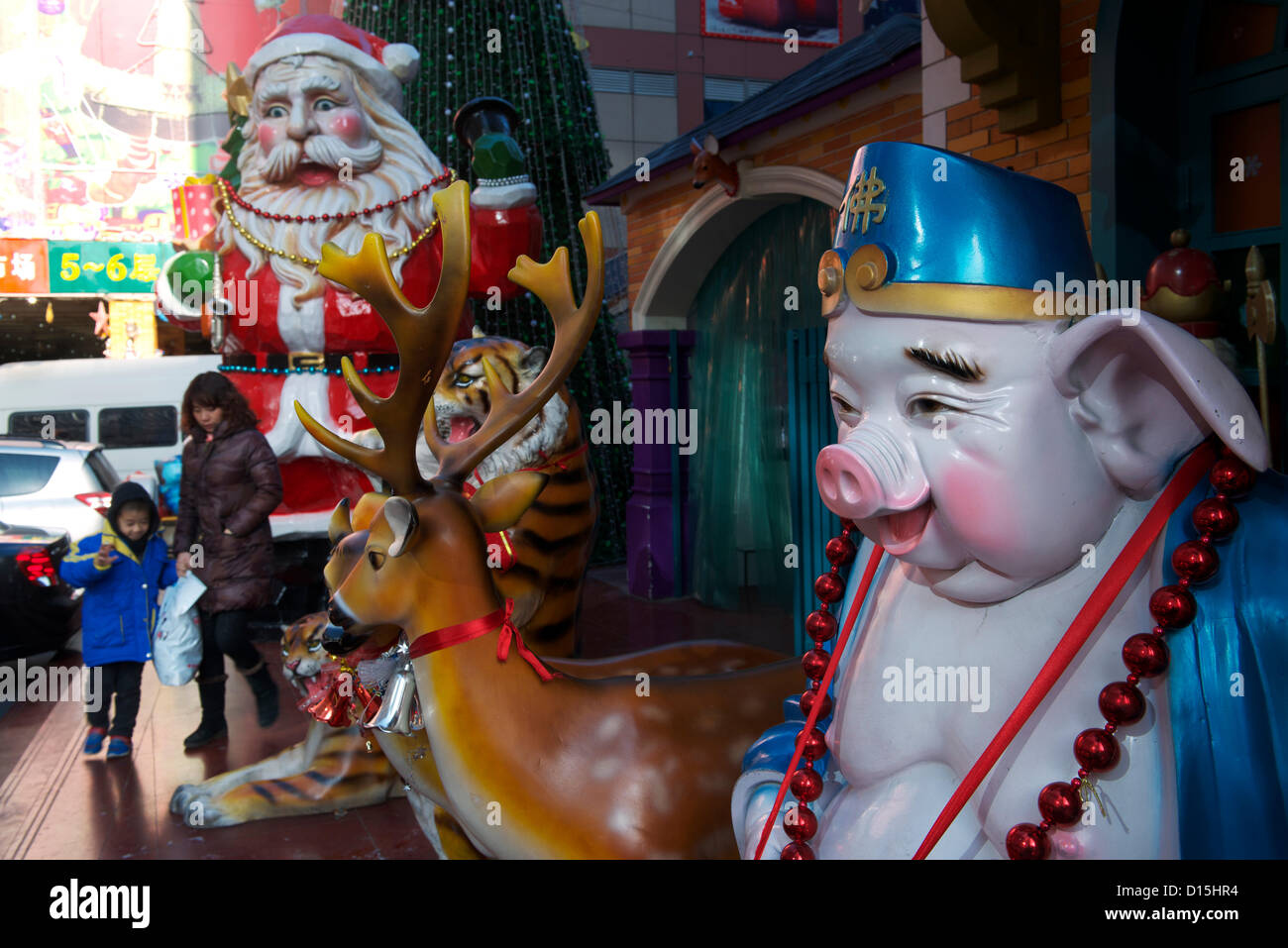 Chinese mother and her son walk along a huge Santa Claus and a statue of Zhu Bajie(Pigsy or Pig), which is one of the three helpers of Xuanzang in the classic Chinese novel Journey to the West outside a commodity market on December 8, 2012 in Beijing, China. Stock Photo