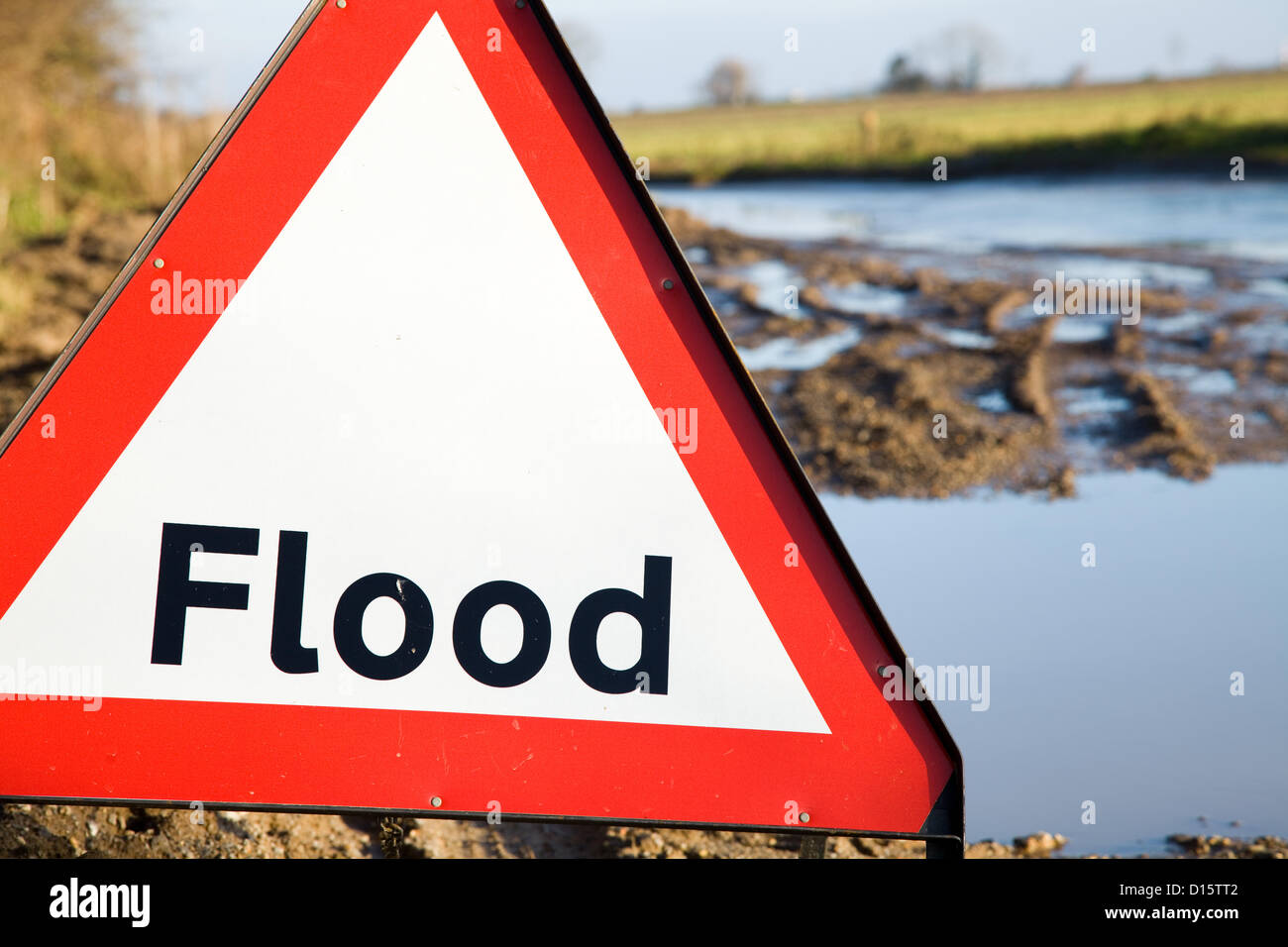 A Flood warning sign next to the road with flood waters just behind it. Stock Photo