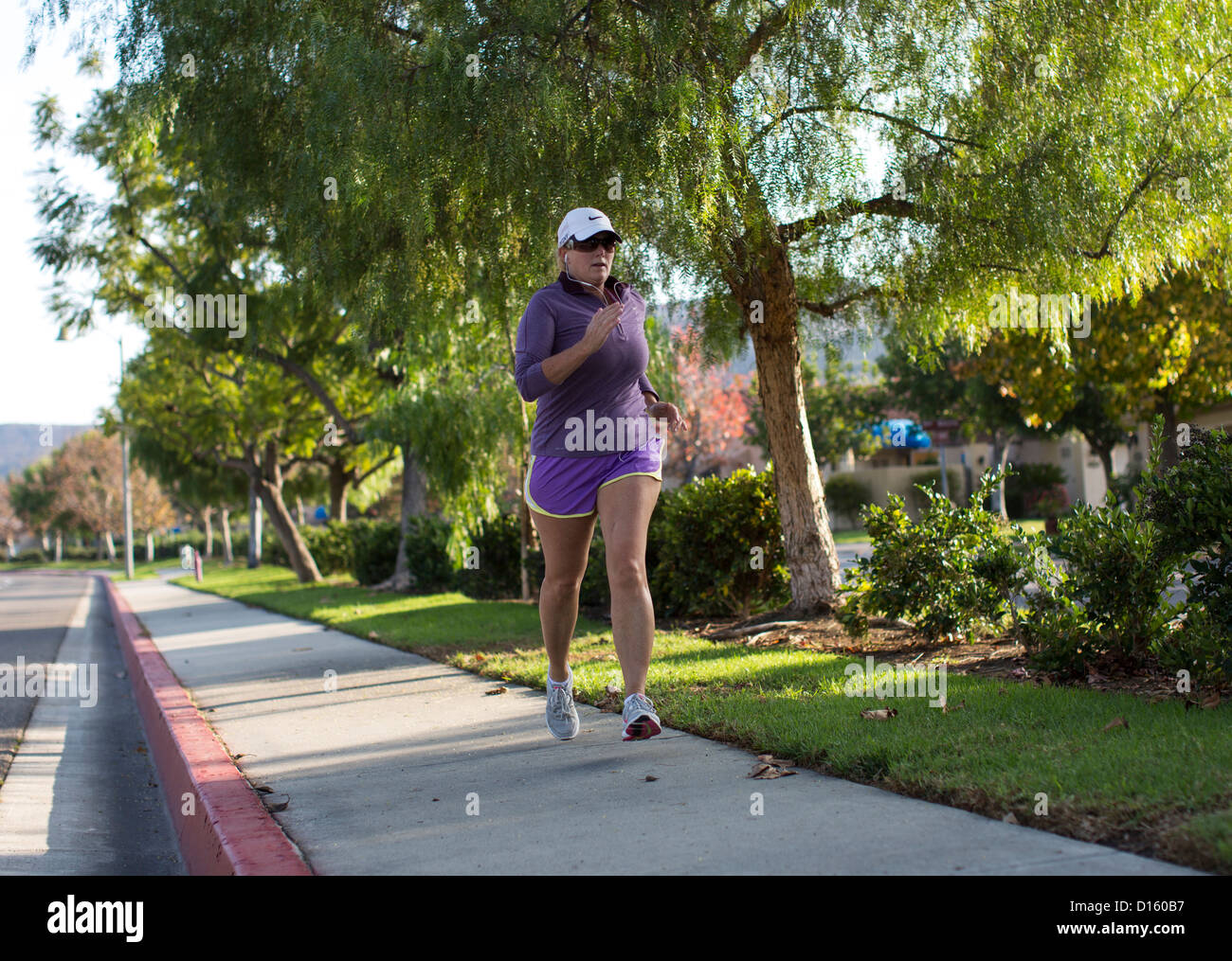 A woman jogs on a sidewalk in San Juan Capistrano, California Stock
