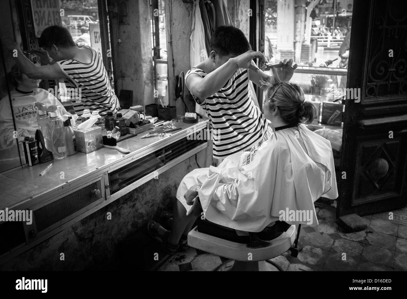 Female traveller having her hair cut in a back street Vietnamese hairdressers in Hanoi's Old Quarter. Stock Photo