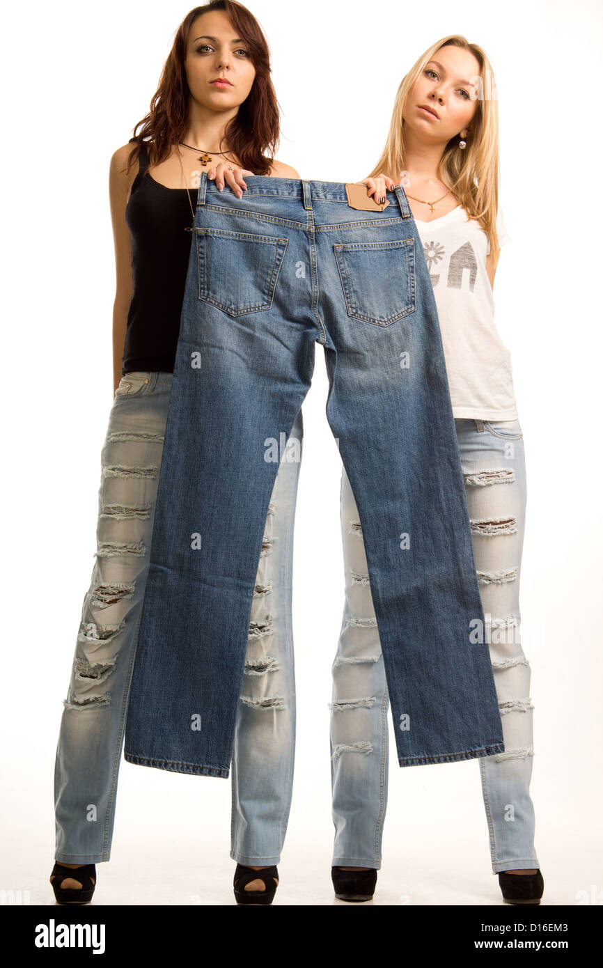 Two young girls dressed in trendy jeans with holes in them holding up a  pair of blue denim jeans together with sulky expressions Stock Photo - Alamy