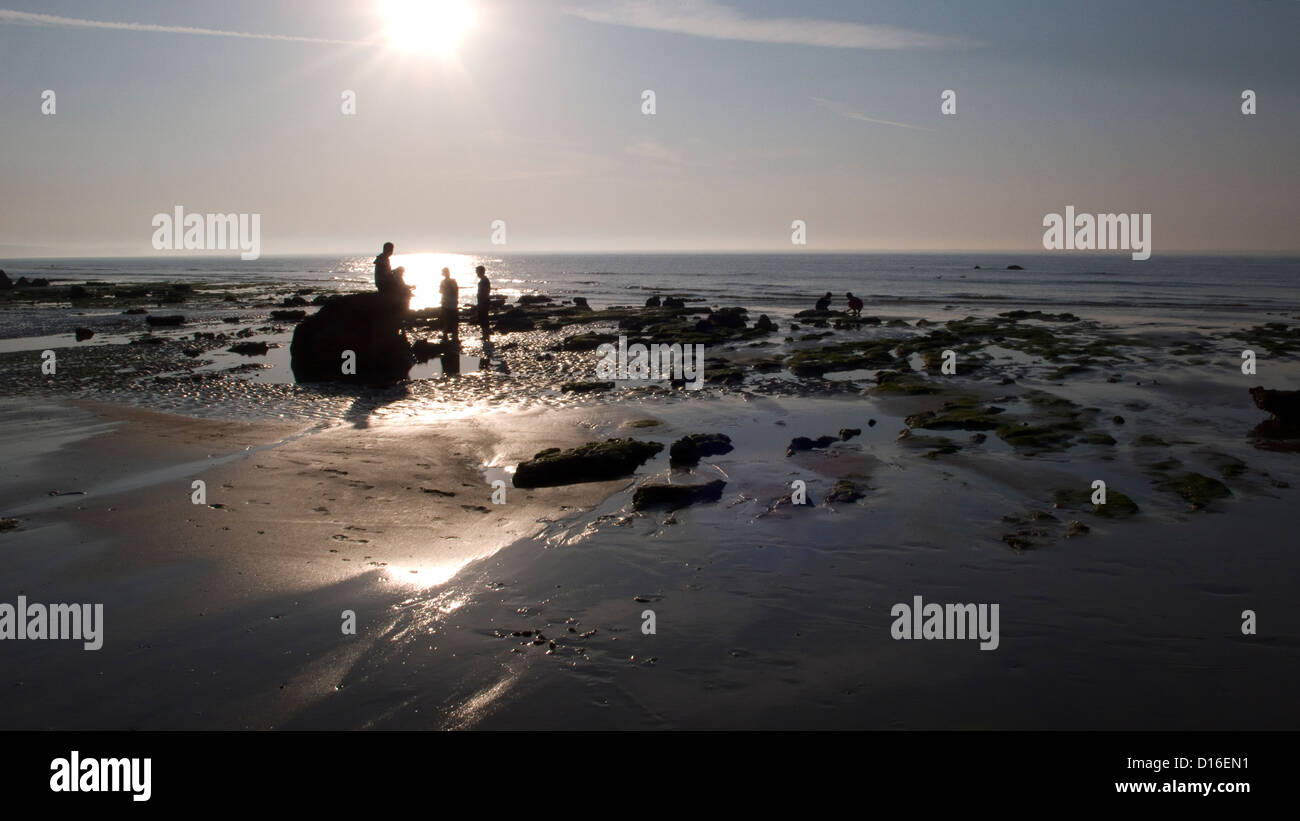 Empty beach, rockpools figures silhouetted against low evening sun Stock Photo