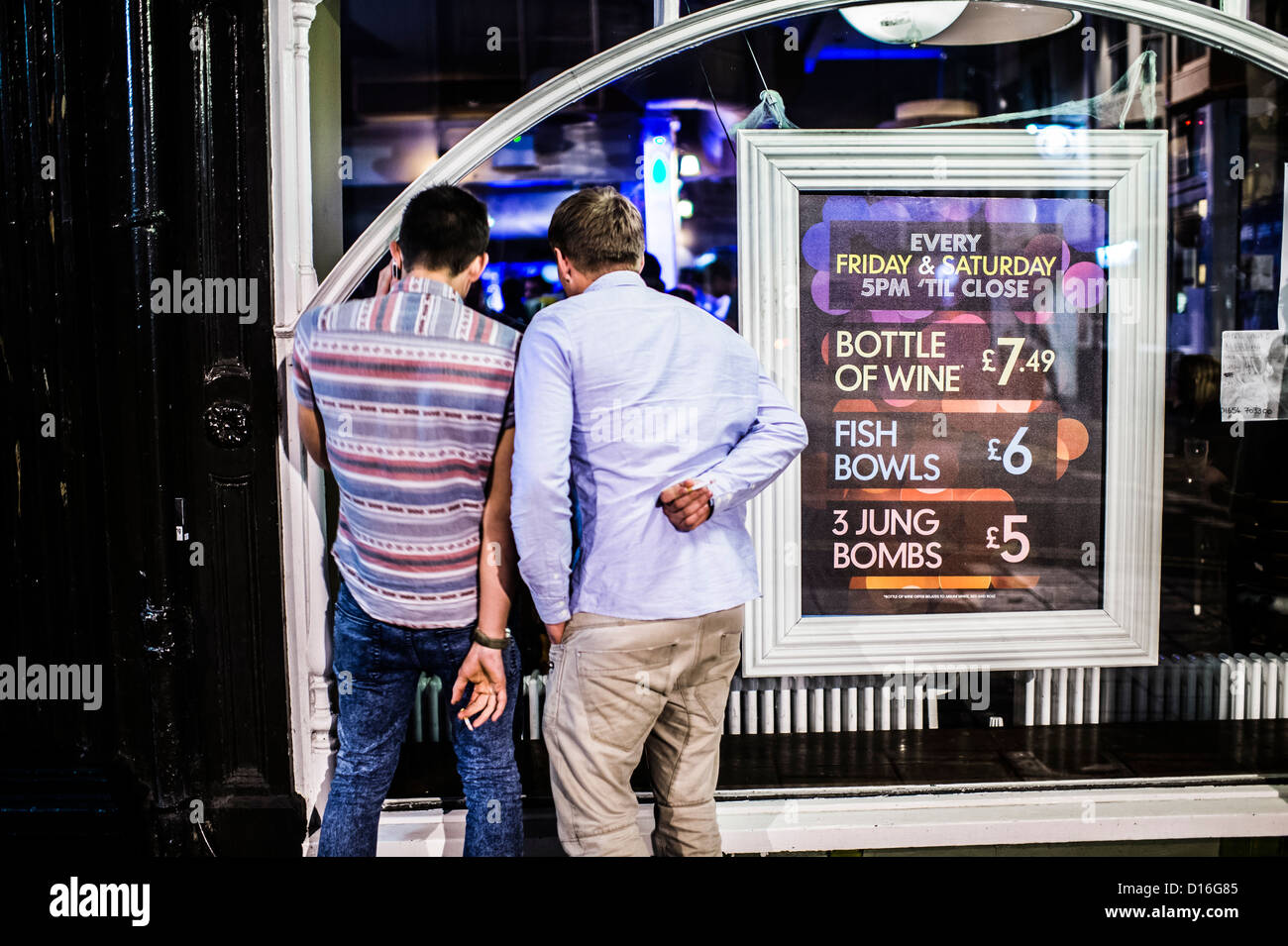 Rear view of Two men looking in a pub club bar  window showing drinks prices on a Saturday night, Aberystwyth Wales UK Stock Photo