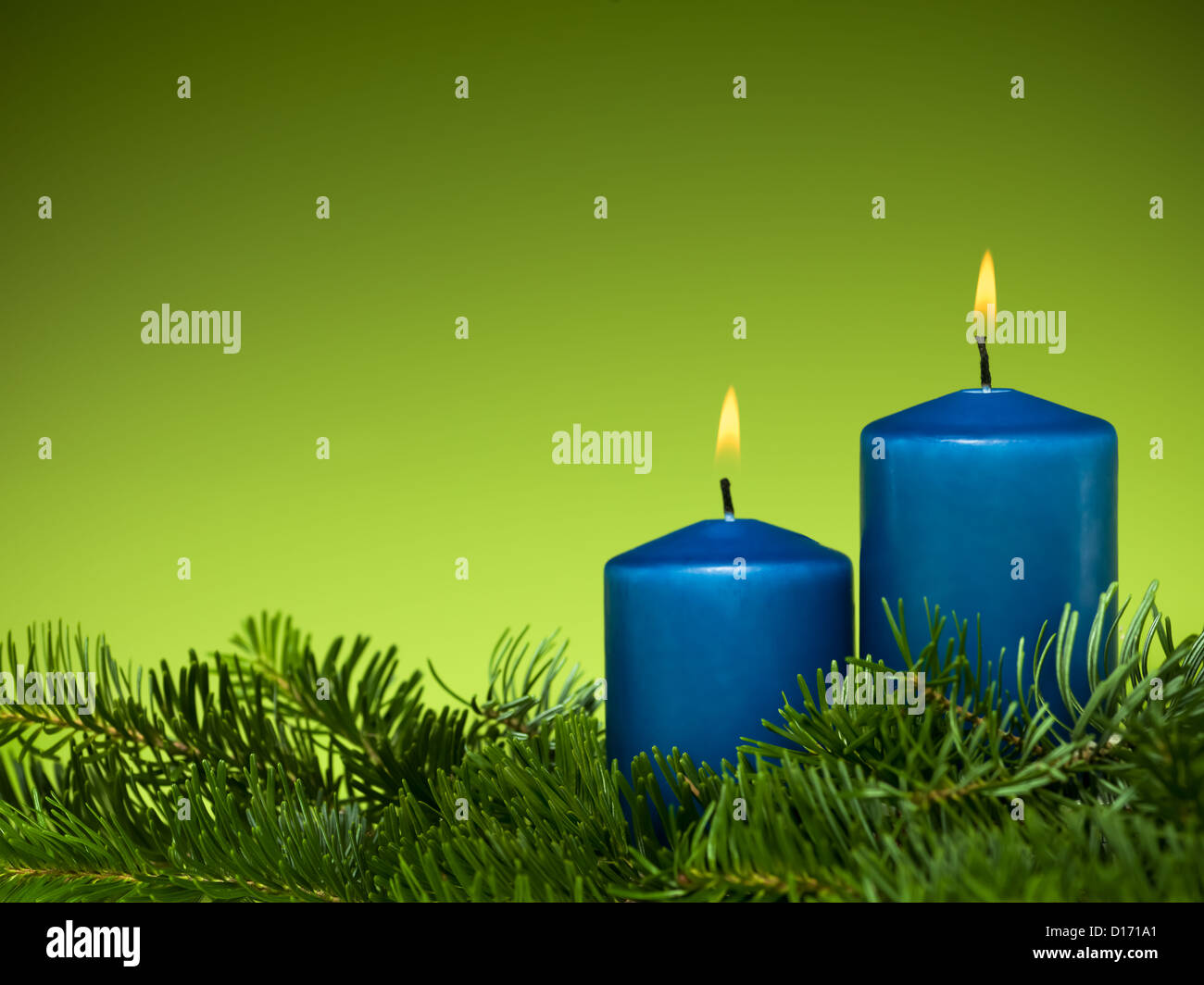 closeup of two burning blue candles surrounded by green fir branches on green background Stock Photo