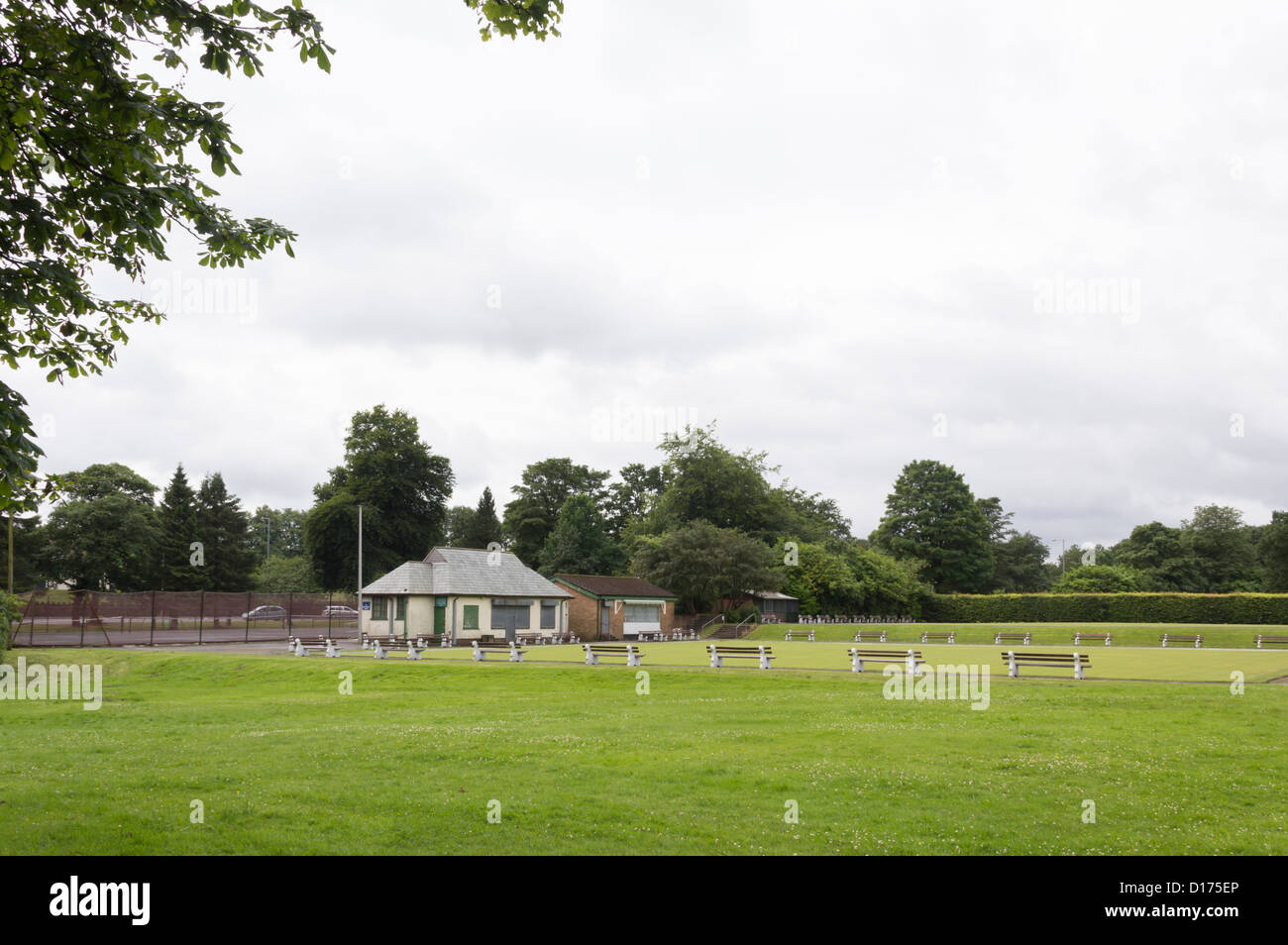 Pavilion and crown bowling green surrounded by bench seats at Moss Bank Park Bolton with tennis courts and Moss Bank Way behind. Stock Photo