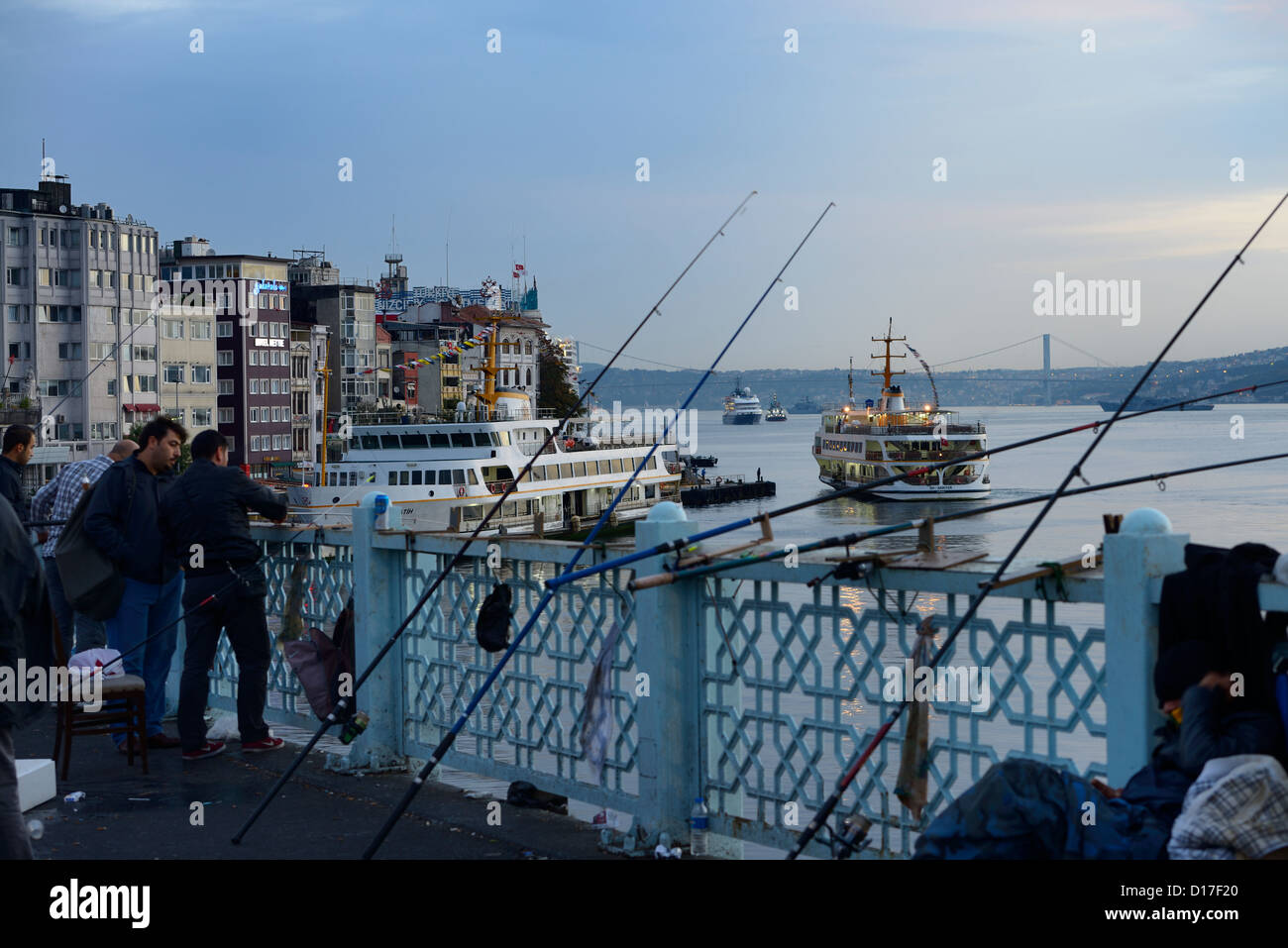 Turkish men fishing on Galata Bridge with Karakoy Pier and early morning sea bus on Boshphorus Istanbul Stock Photo