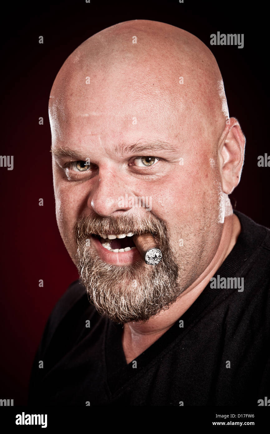 bald man with a beard smokes a cigar Stock Photo