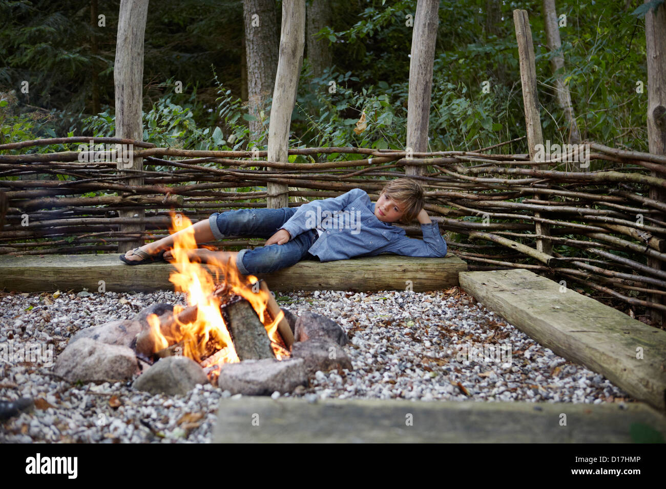 Boy relaxing by fire outdoors Stock Photo