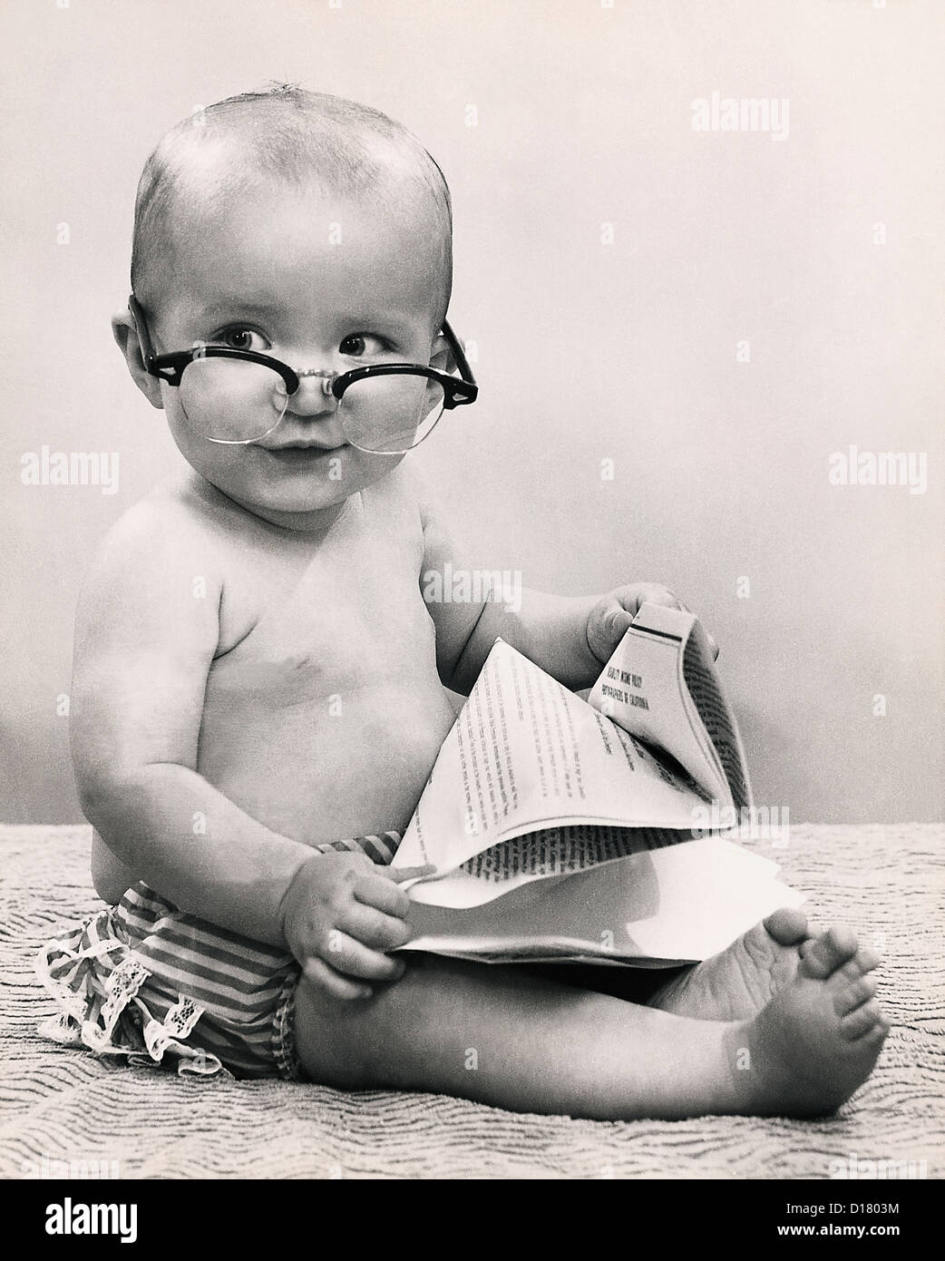Baby wearing eyeglasses and holding paper Stock Photo