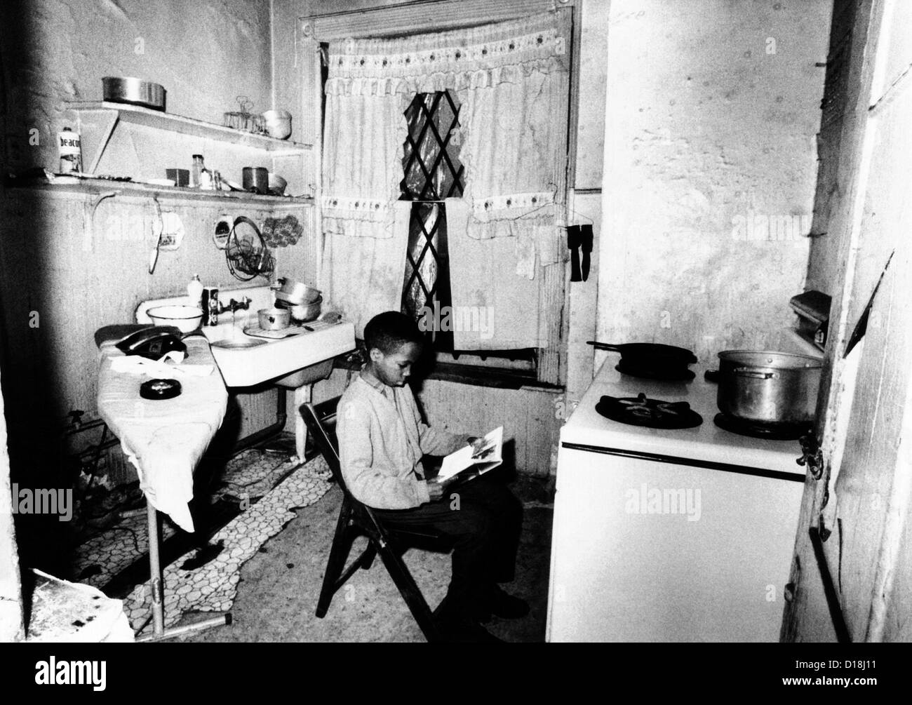 African American youth studies by the kitchen stove because his apartment, like the others in his buildings, is without heat. Stock Photo