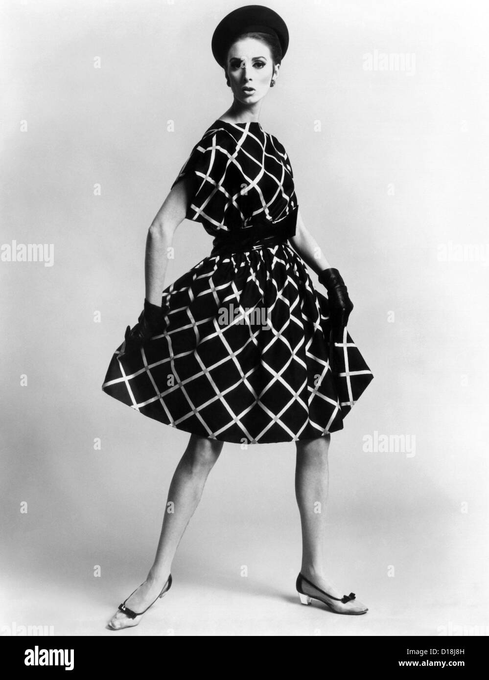 Dress by Pauline Trigere. Short and full skirted dress with a loose draped bodice. The model wears low heeled shoes that Stock Photo
