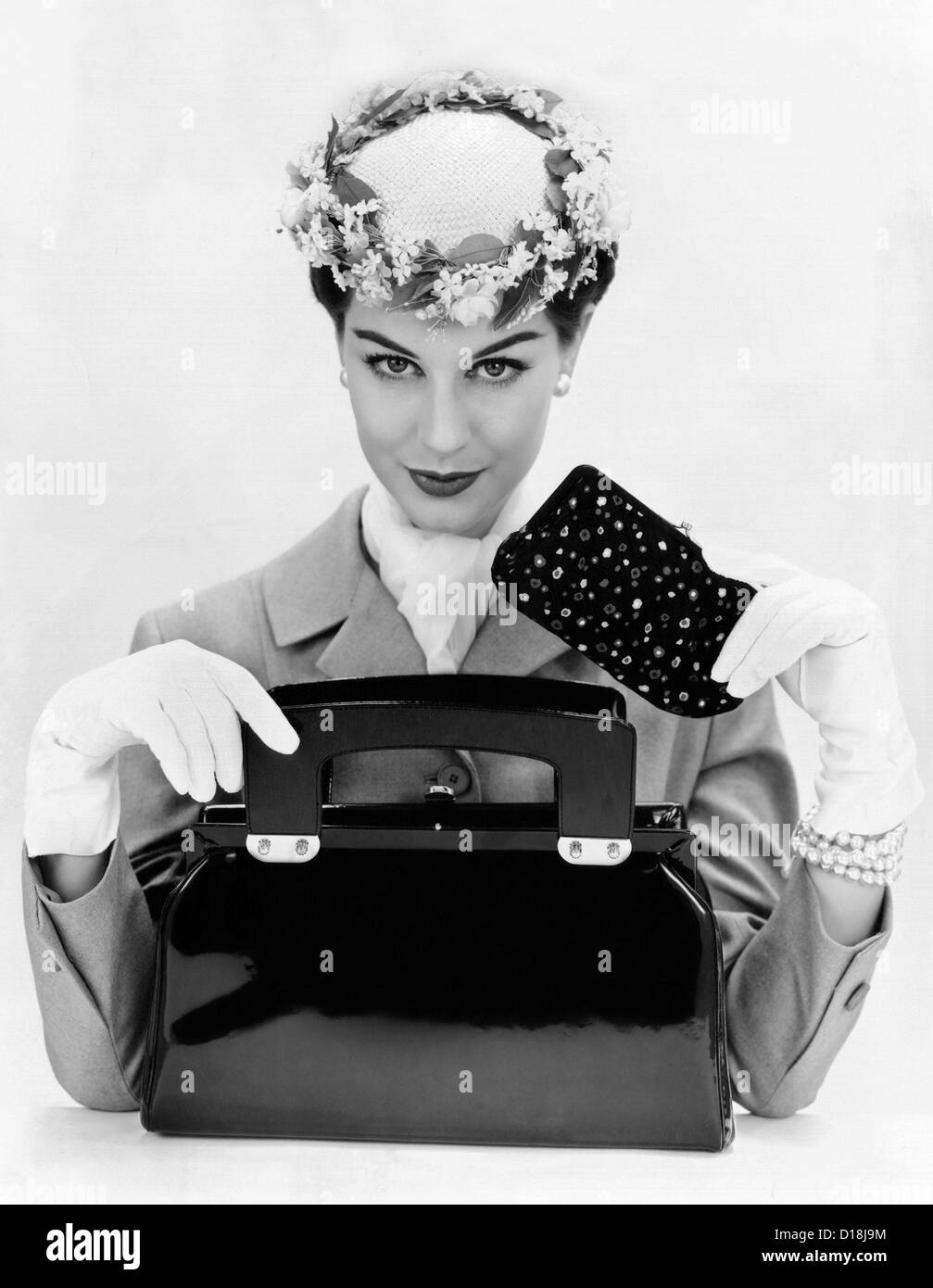 Women's accessories include a square cut, top opening, black patent leather purse. A small forward worn hat with floral edging Stock Photo