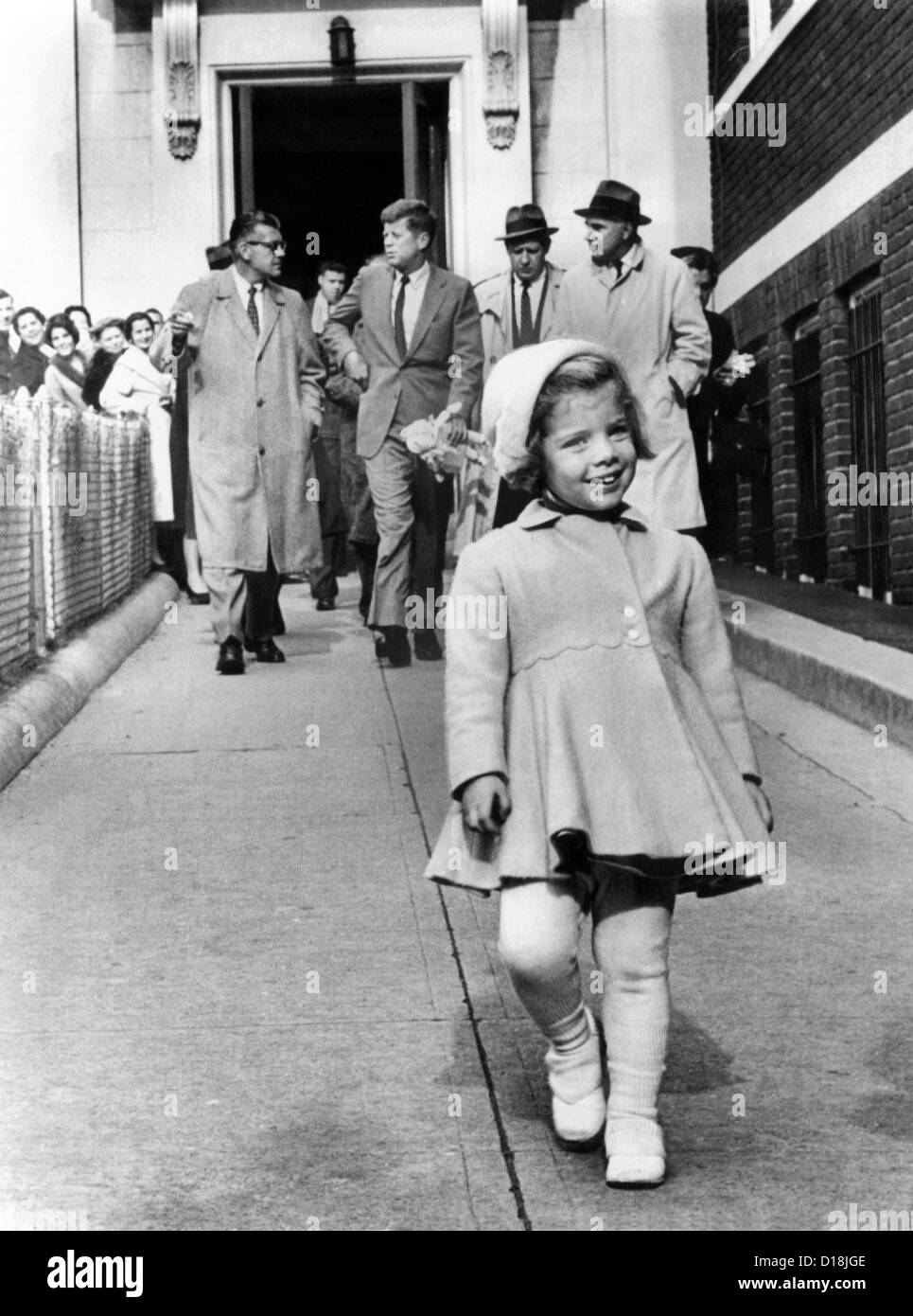 Caroline Kennedy on her third birthday. In the background, her father, President -elect John Kennedy holds her doll as he walks Stock Photo