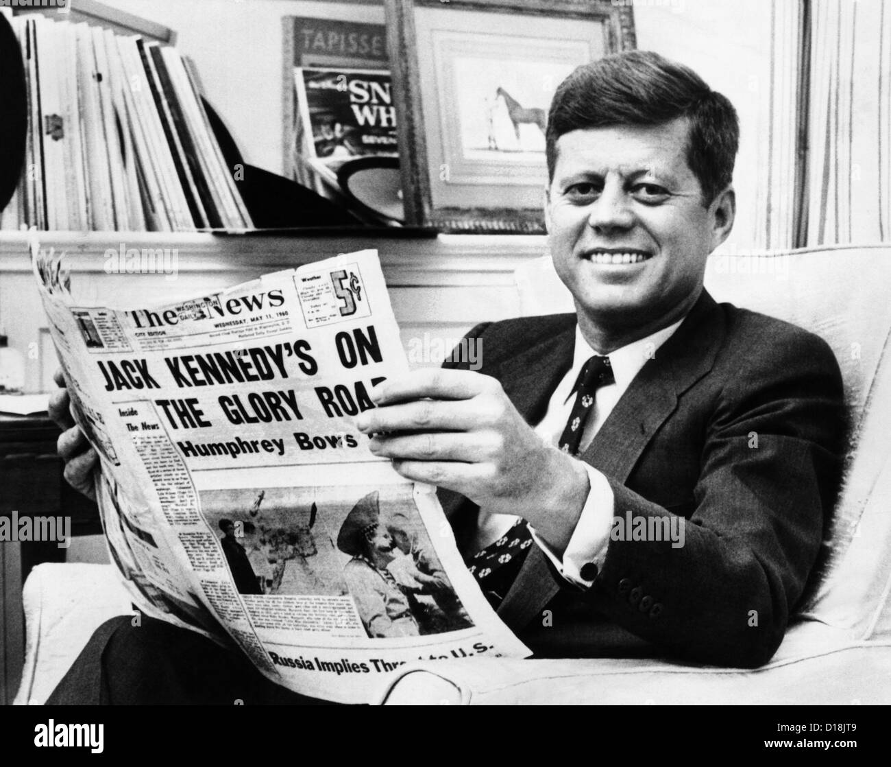 Sen. John Kennedy becomes the front-runner for the 1960 Democratic Presidential Nomination. He smiles while reading a newspaper Stock Photo